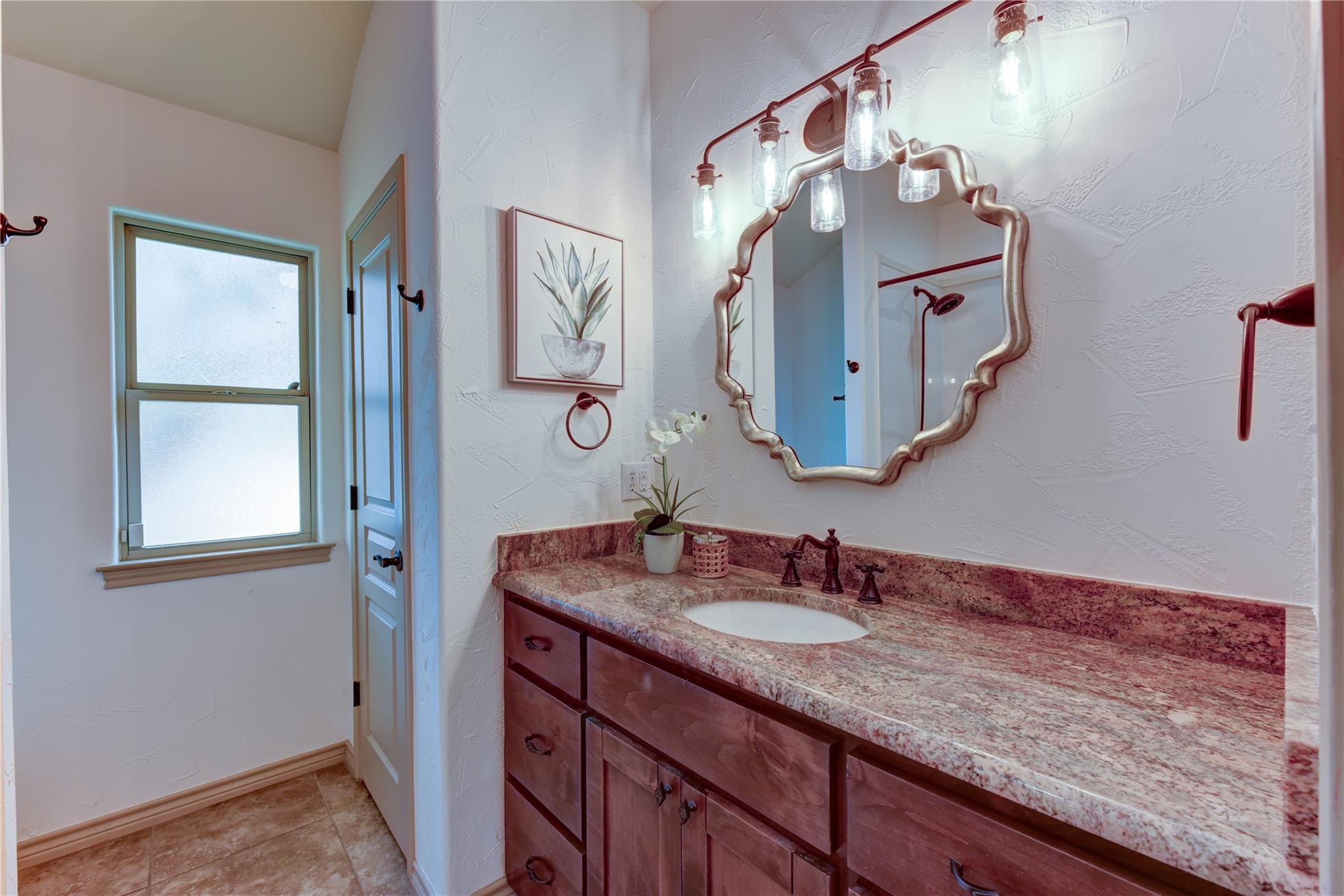 Bathroom vanity with a stone countertop, dark wood cabinets, and an ornate mirror.