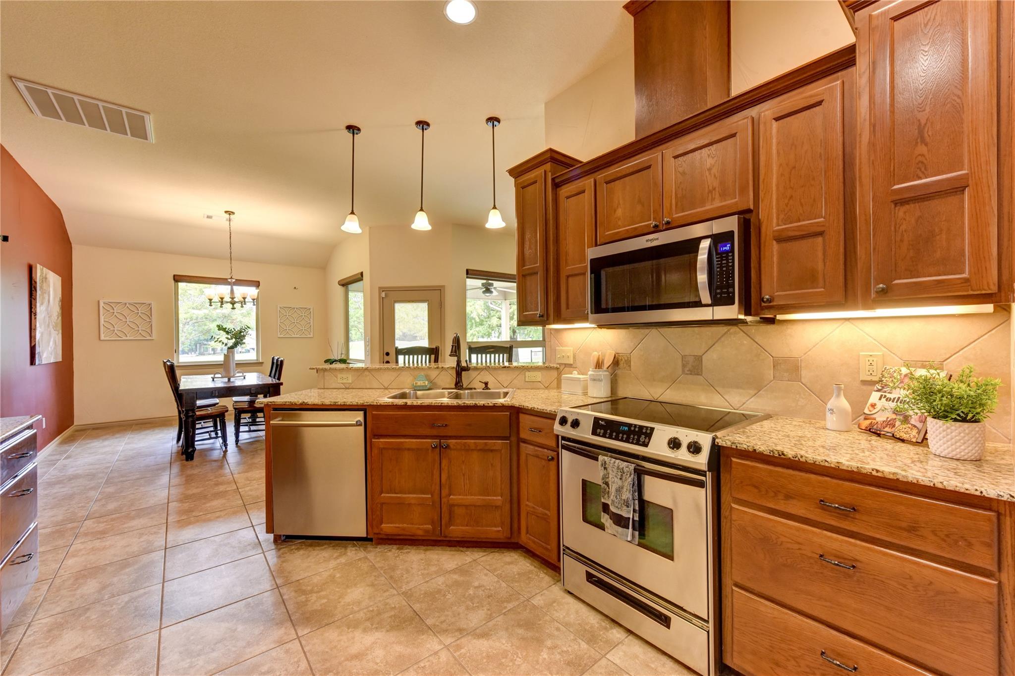 Kitchen with warm wood cabinets, granite counters, stainless steel appliances, and a dining area beyond.