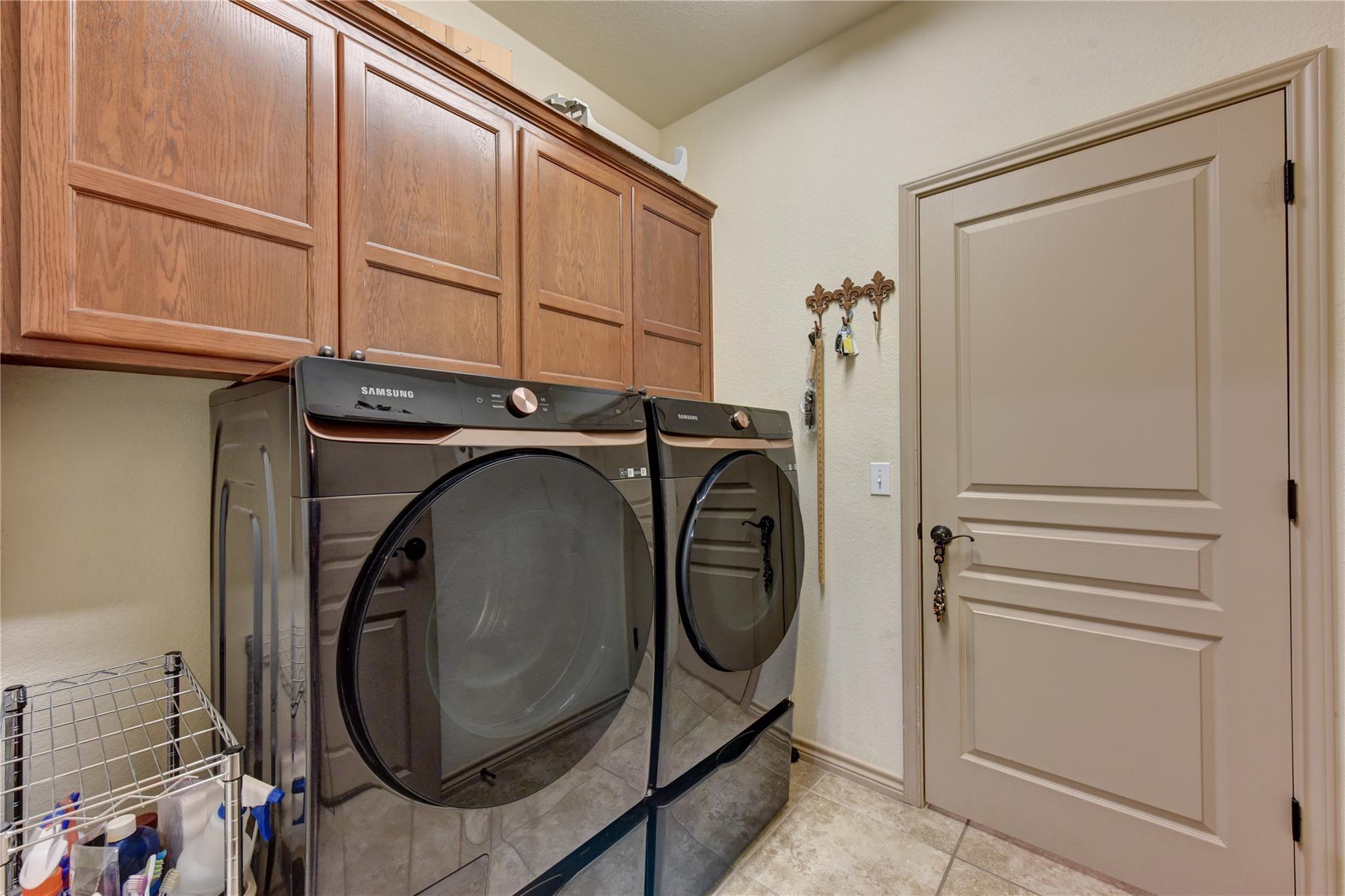Laundry room with dark front-loading washer and dryer beneath wood cabinets.