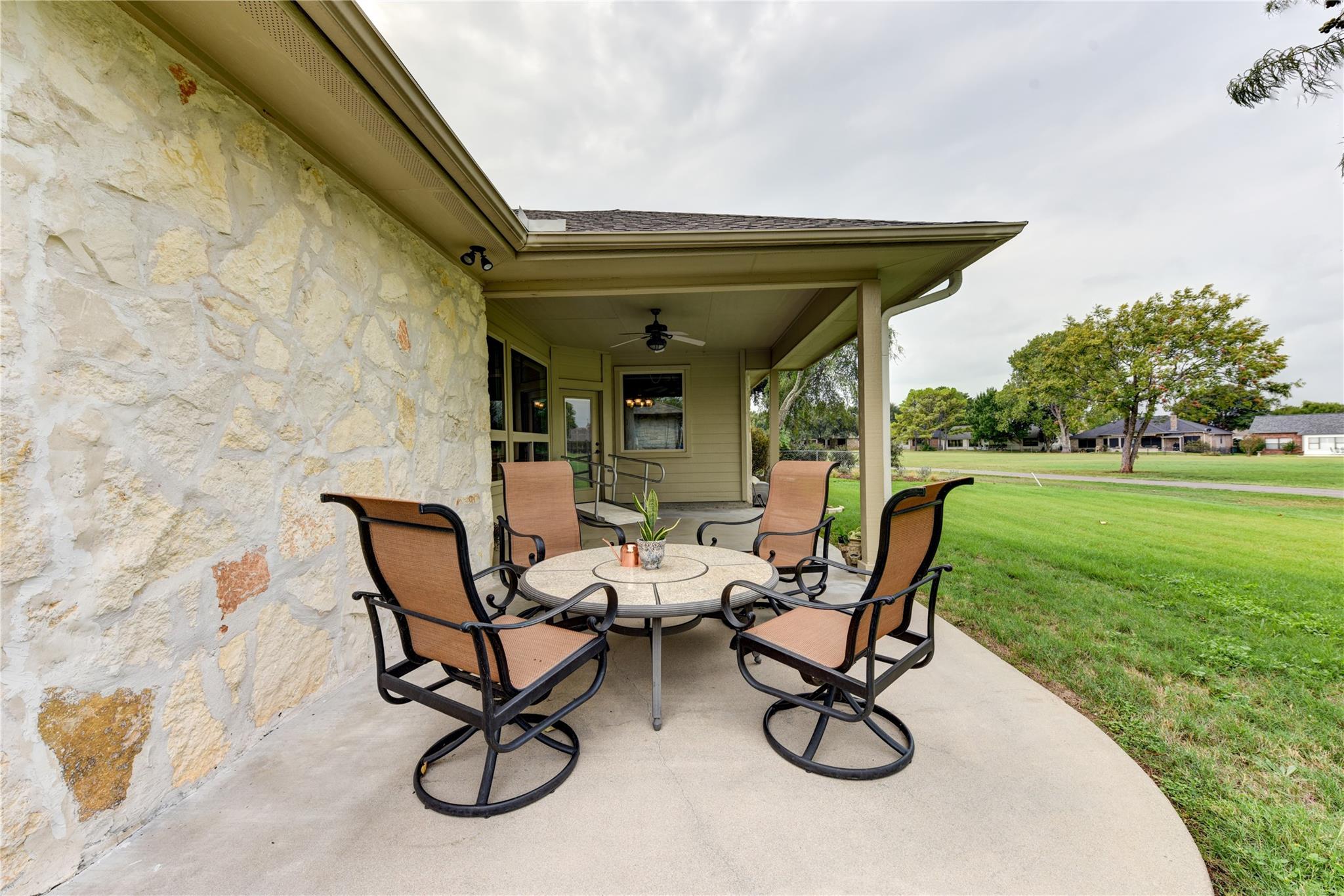 Covered stone-house patio with a round table and four chairs overlooking a green lawn.