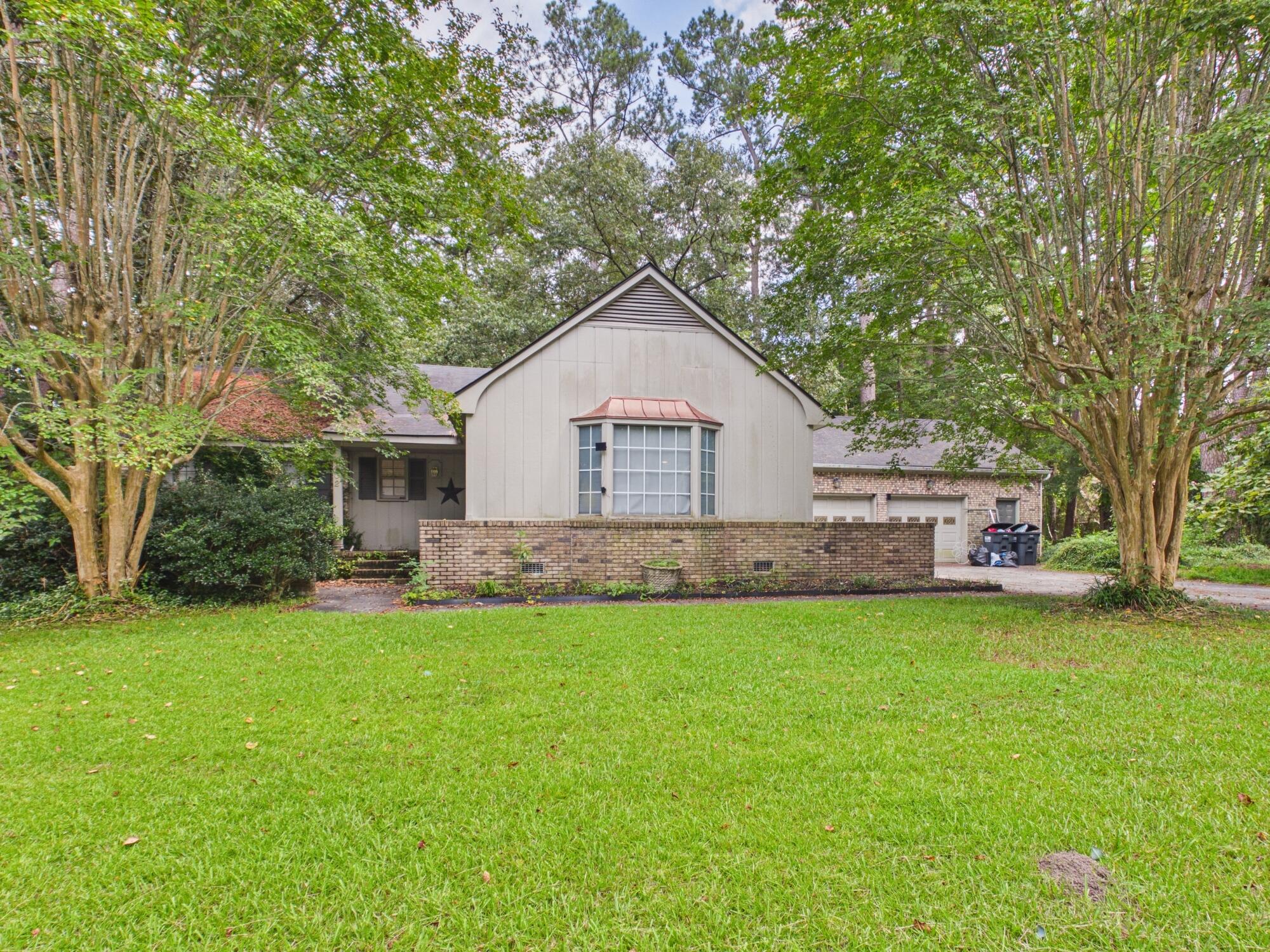 Gabled house with a large bay window, brick front wall, and broad lawn beneath mature trees.