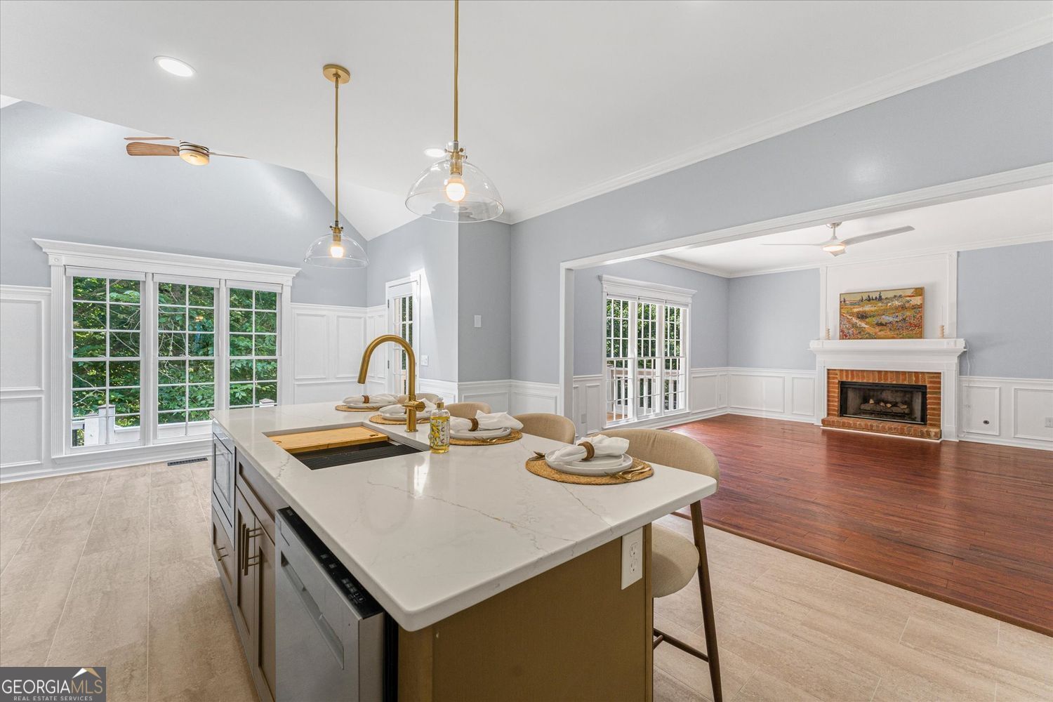 Kitchen with a large stone island opening to a living room with hardwood floors and a brick fireplace.