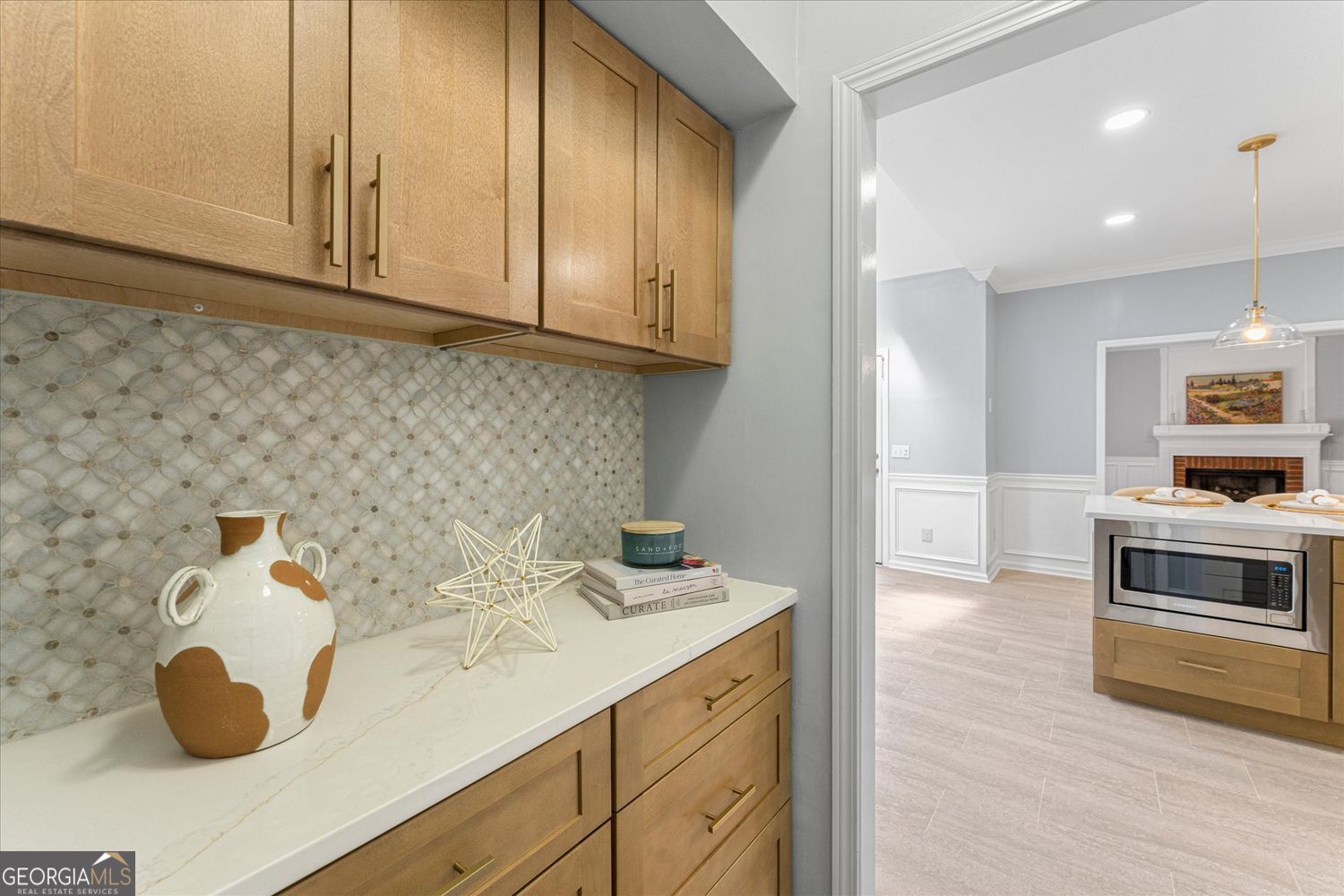 Kitchen with light wood cabinetry, patterned tile backsplash, and an adjoining room with a fireplace.