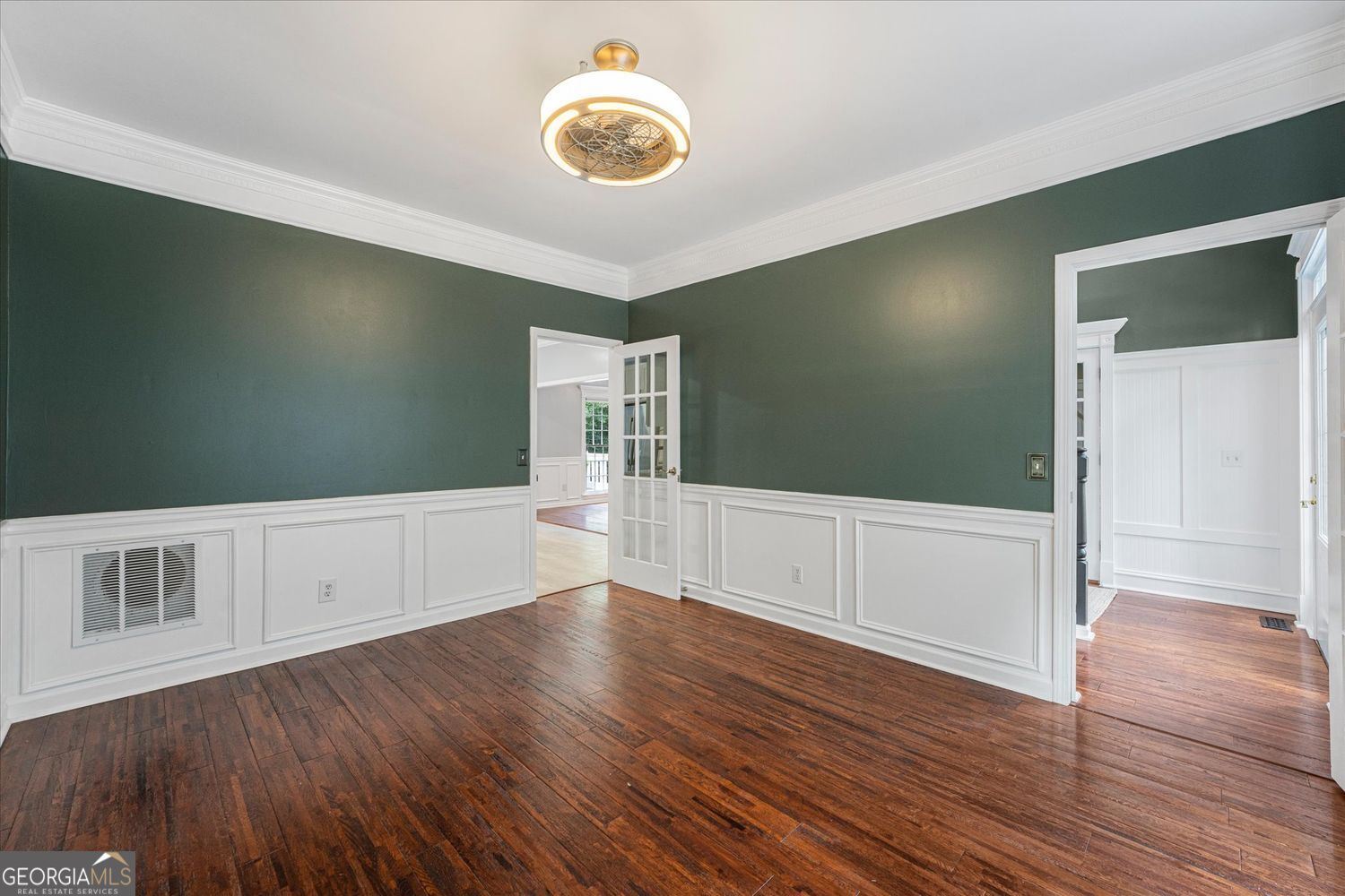Empty room with green walls, white wainscoting, hardwood floors, and a ceiling light.
