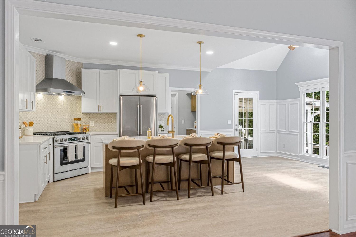 Bright kitchen with white cabinets, stainless steel appliances, and a large island with four stools.