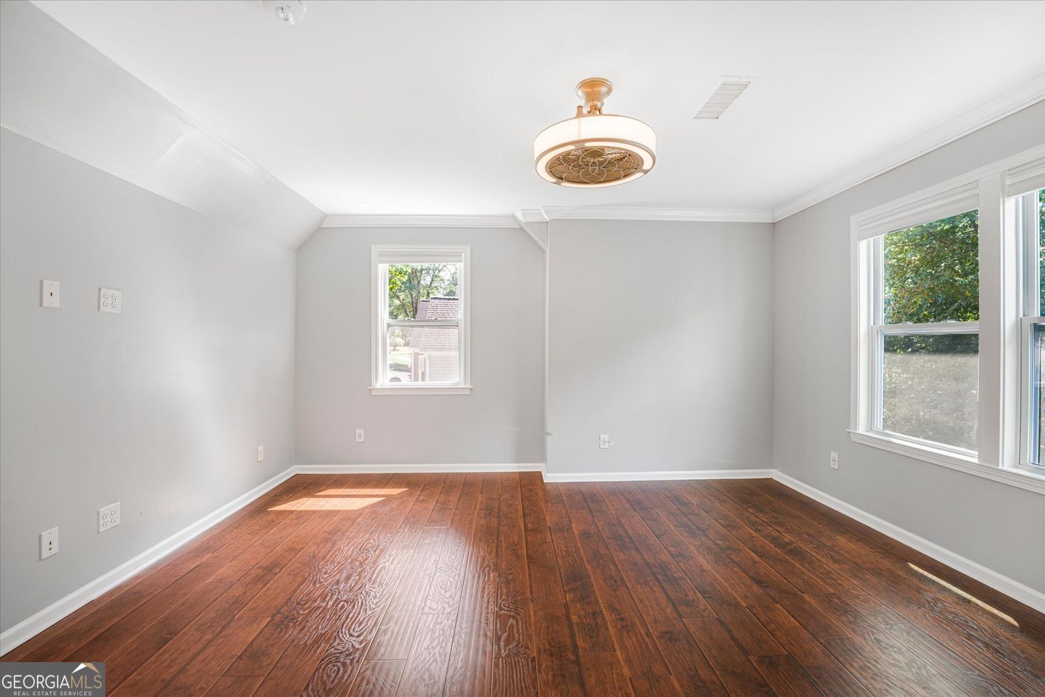 Vacant room with reddish-brown hardwood floors, gray walls, and three windows.