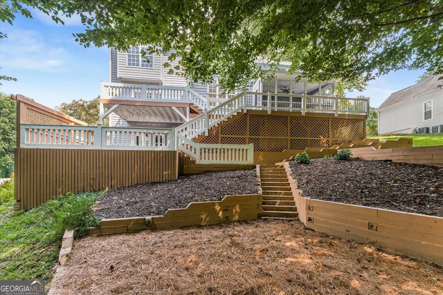 Rear of a gray two-story home with a multilevel deck and terraced backyard stairs.