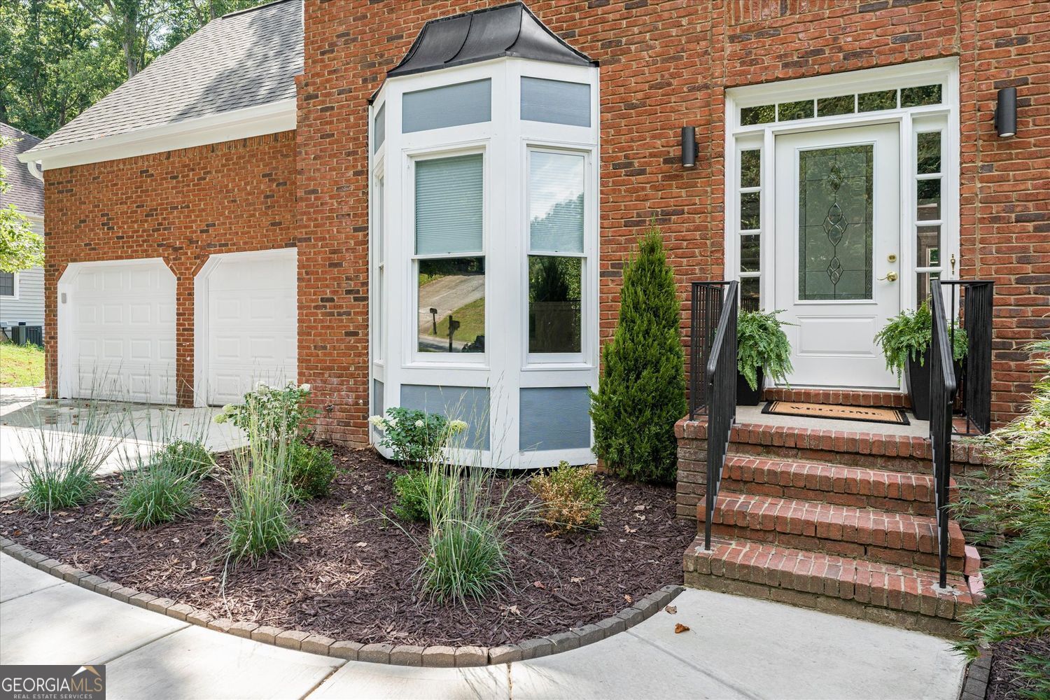 Red brick home with a white bay window, double garage, and raised front entry steps.