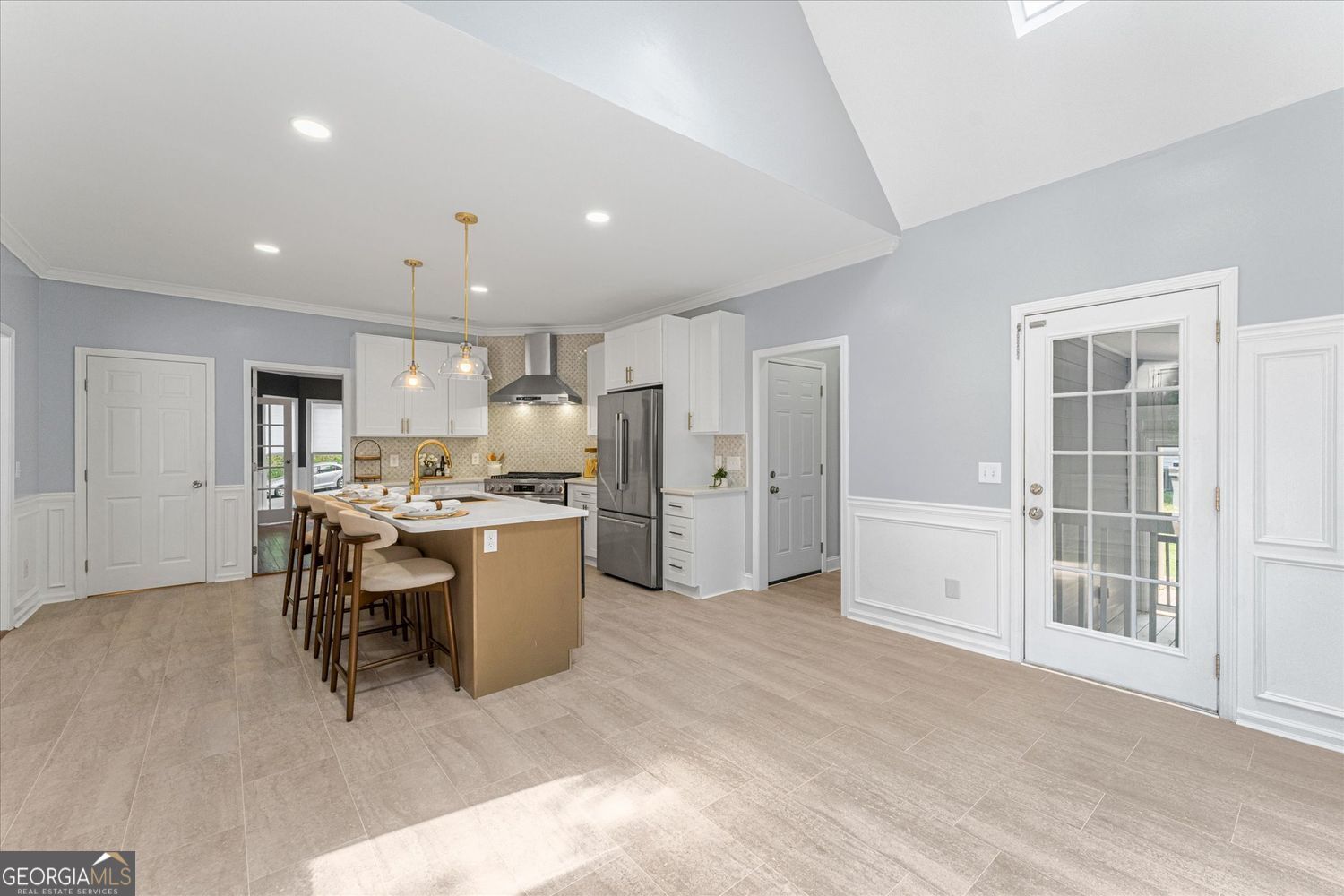 Open kitchen with a tan island, white cabinets, stainless steel appliances, and light tile flooring.