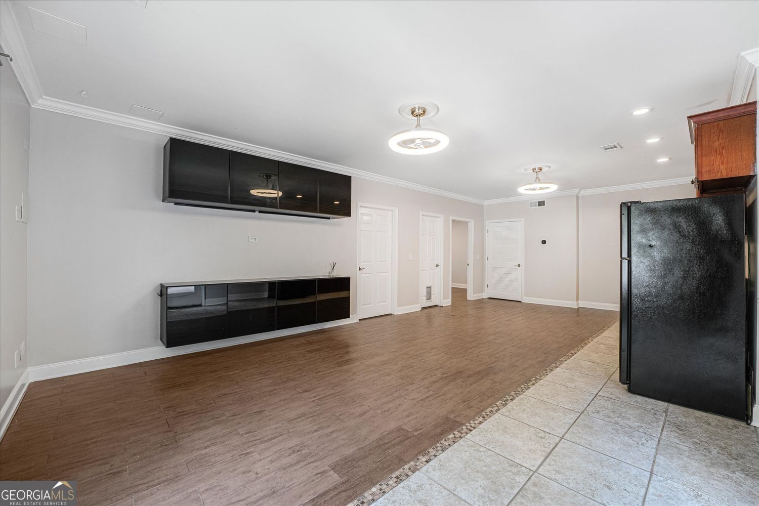 Kitchen and dining area with dark cabinetry, a black refrigerator, and adjoining plank and tile floors.