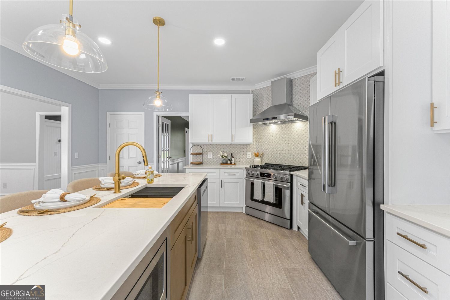 Bright kitchen with white cabinetry, a quartz island, stainless steel appliances, and brass fixtures.