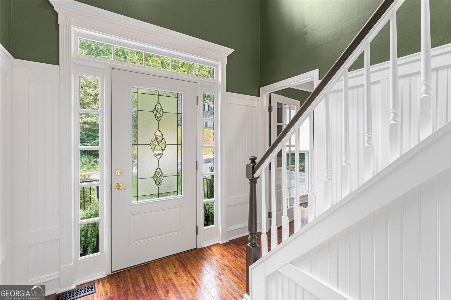 Foyer with a decorative stained-glass front door, polished hardwood floors, and a white staircase.