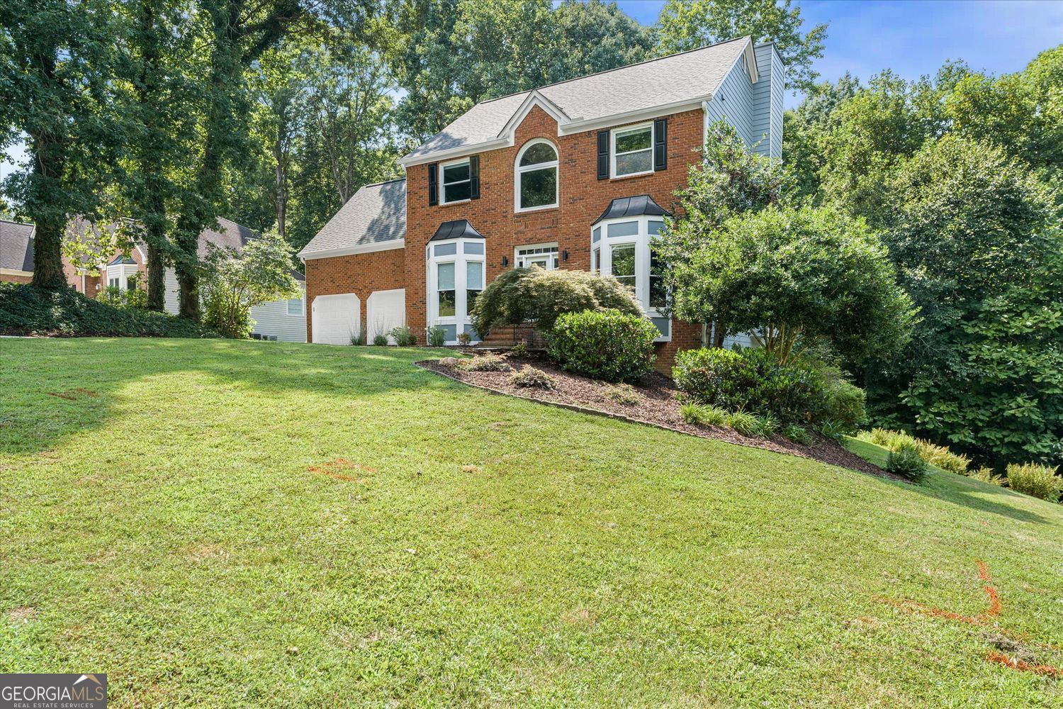 Two-story brick house with bay windows and an attached garage above a broad, sloping lawn.