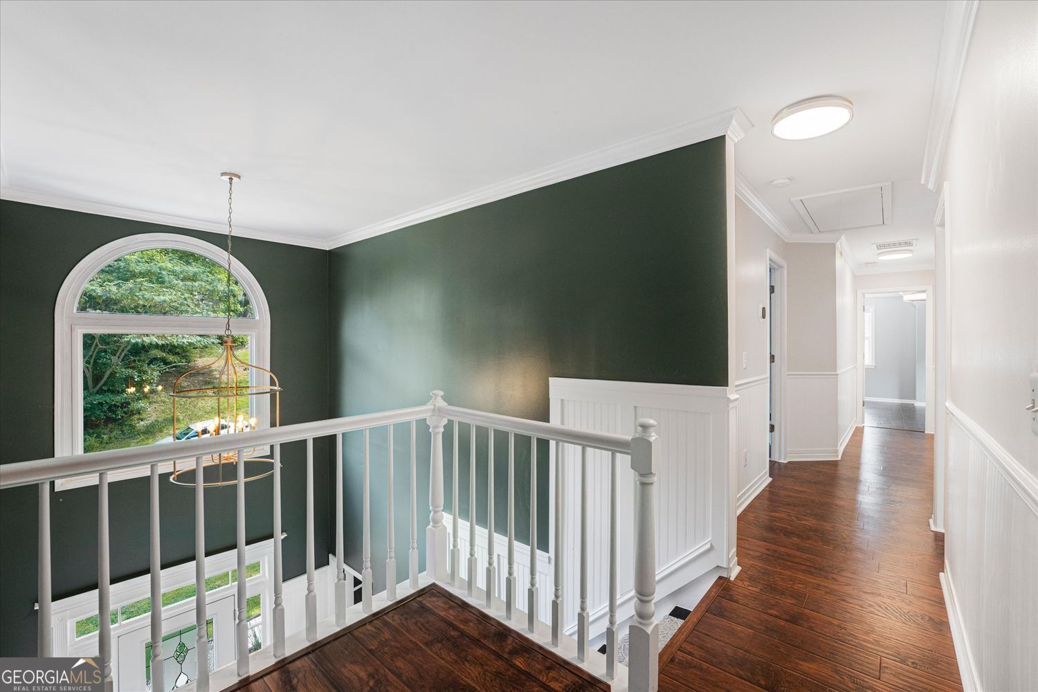 Upstairs landing with dark hardwood floors, white railing, and a large arched window.