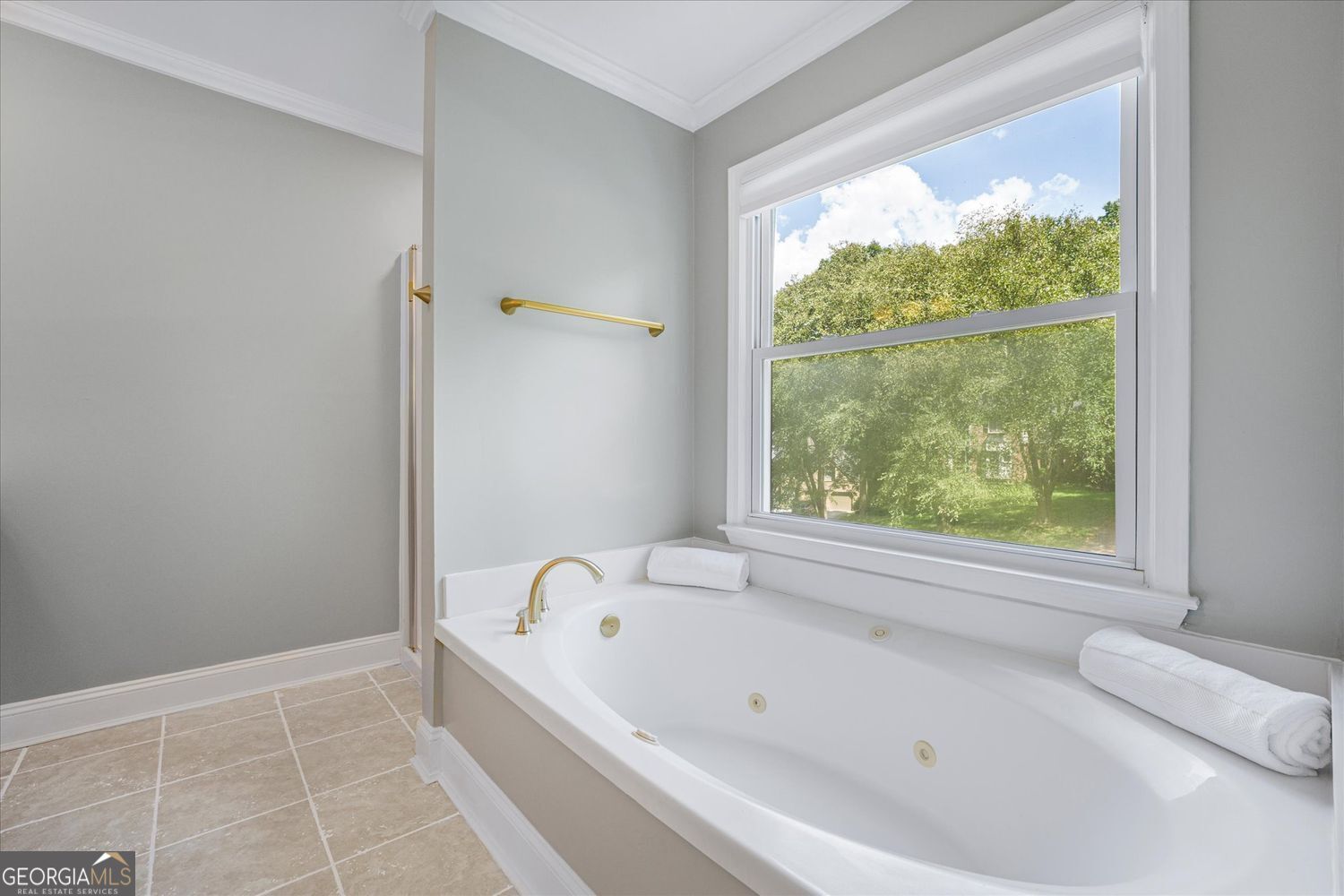 Bathroom with a jetted soaking tub beneath a large window overlooking leafy trees.