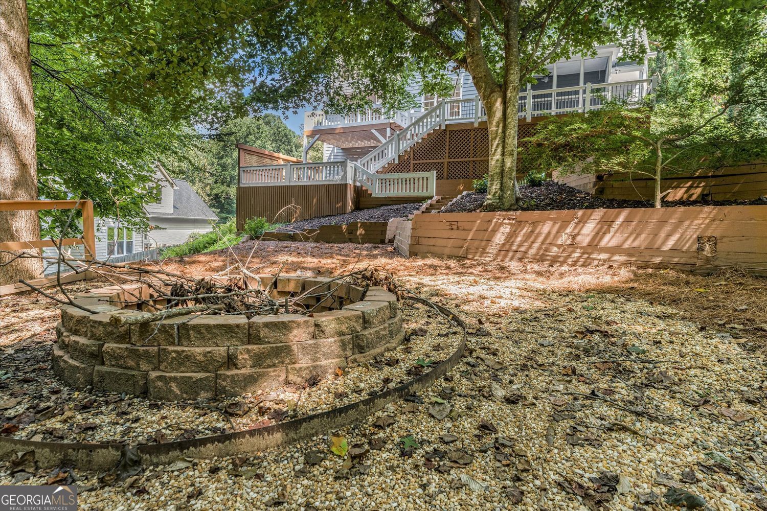 Backyard with a raised deck, tiered retaining walls, and a circular stone fire-pit area.