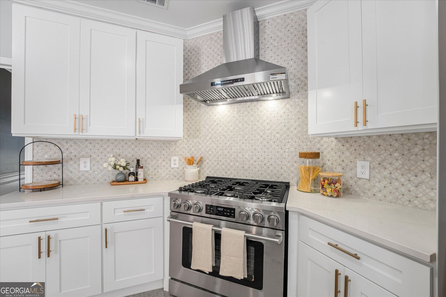 Kitchen with white cabinets, patterned tile backsplash, and stainless-steel gas range and hood.