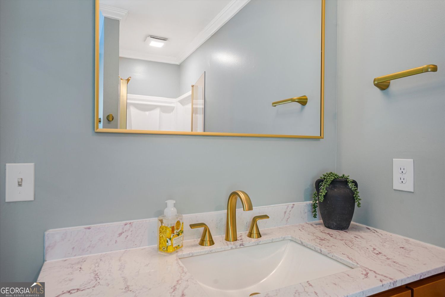 Bathroom vanity with a gold faucet, pink-veined countertop, and large gold-framed mirror.