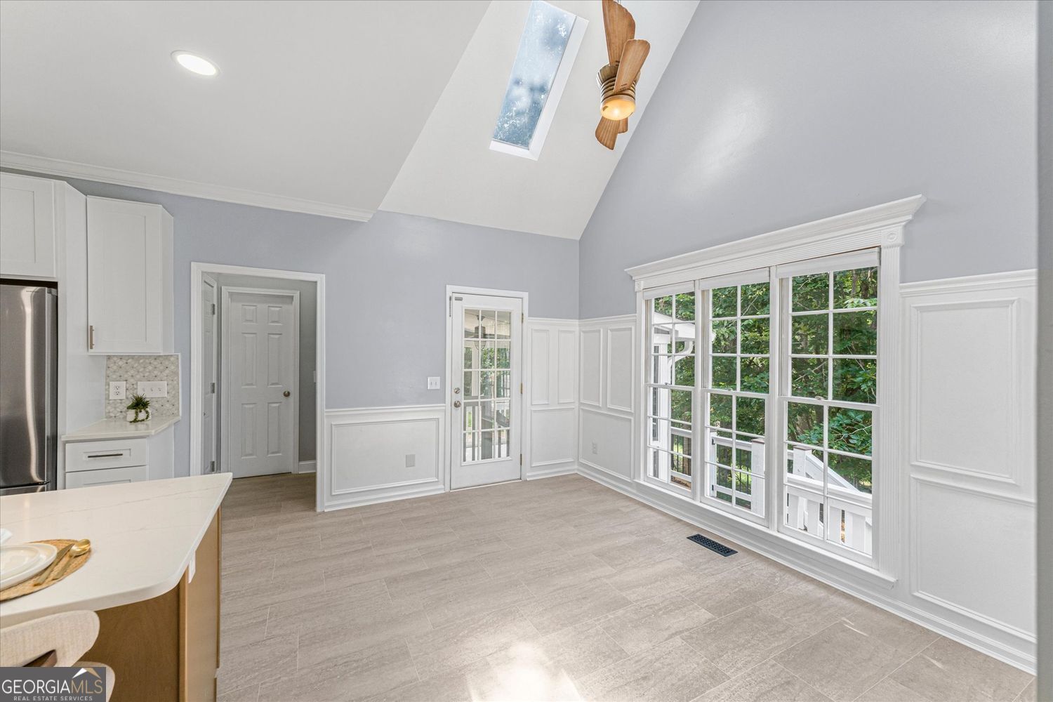 Kitchen and dining area with a skylight, large windows, and white paneled walls.