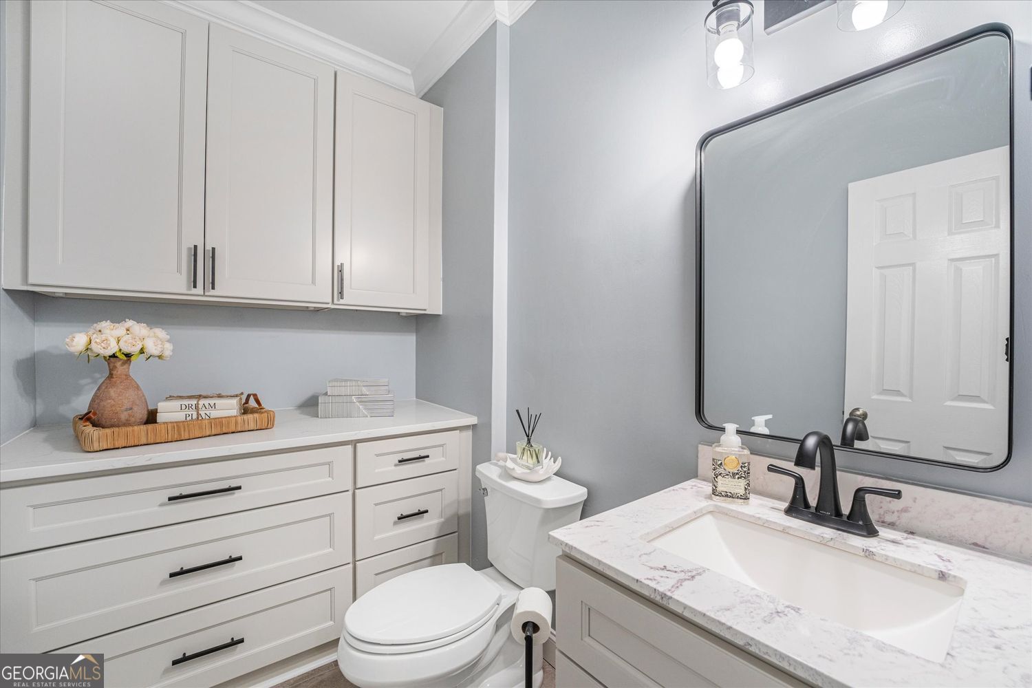 Bathroom with white cabinetry, a marble-look vanity, black faucet, and large framed mirror.