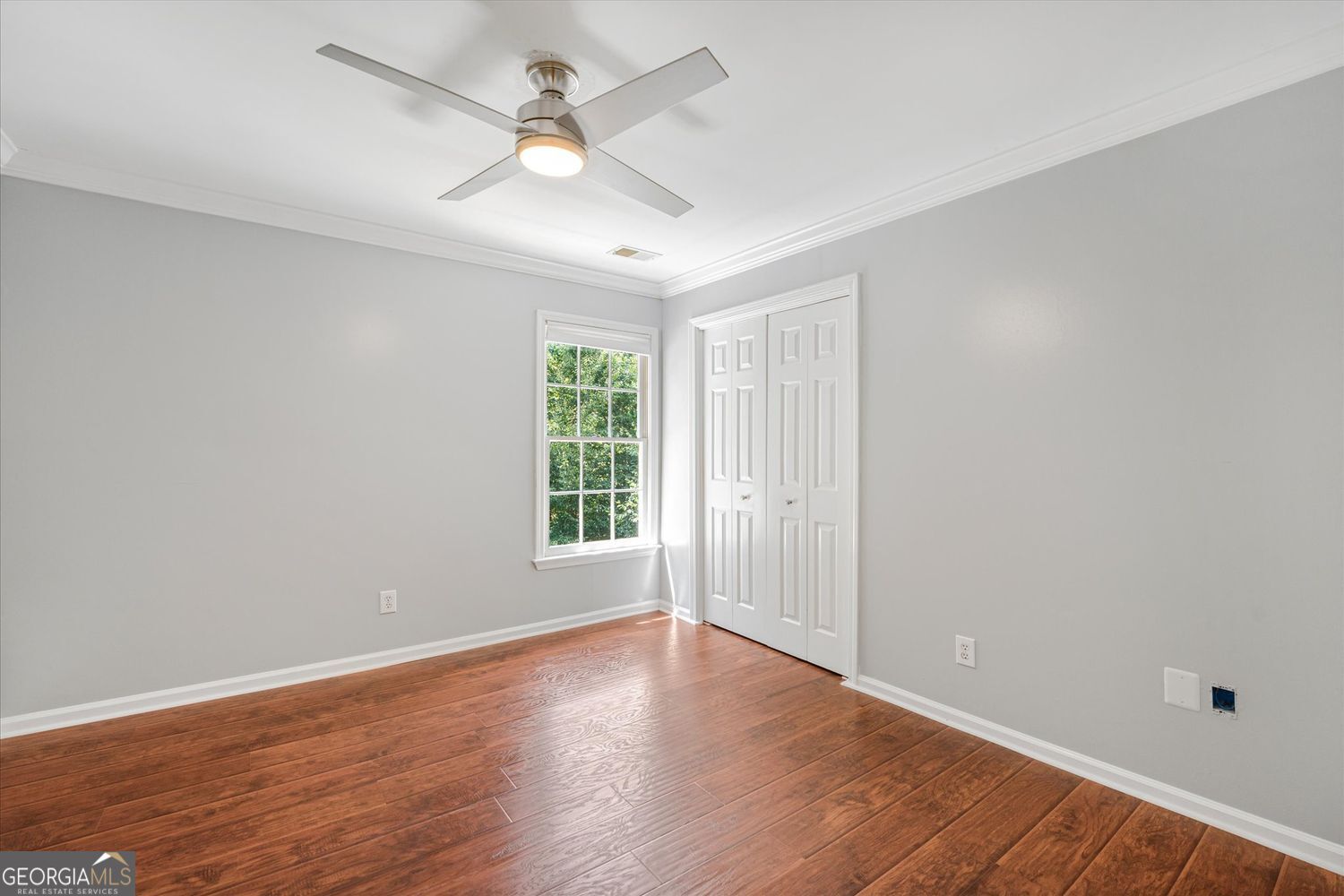 Vacant bedroom with hardwood floors, a ceiling fan, and double closet doors.