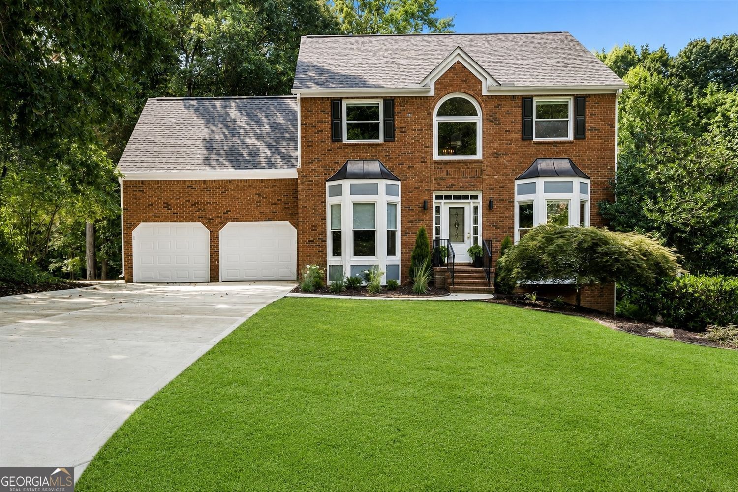 Two-story brick house with bay windows, double garage, wide driveway, and front lawn.