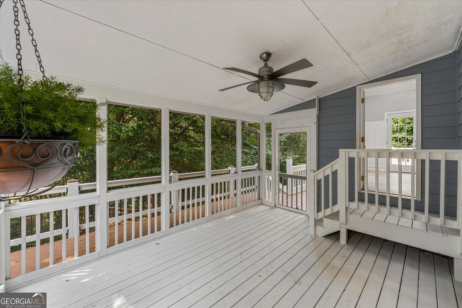 Screened porch with white floors and railings, a ceiling fan, and views of leafy trees.