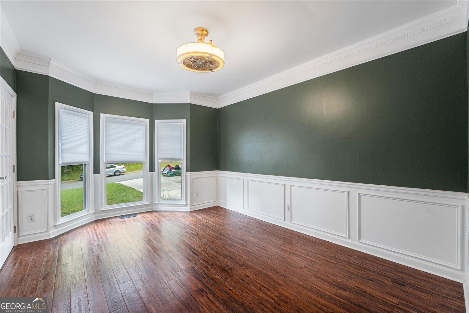 Empty room with dark green walls, white wainscoting, three windows, and hardwood floors.