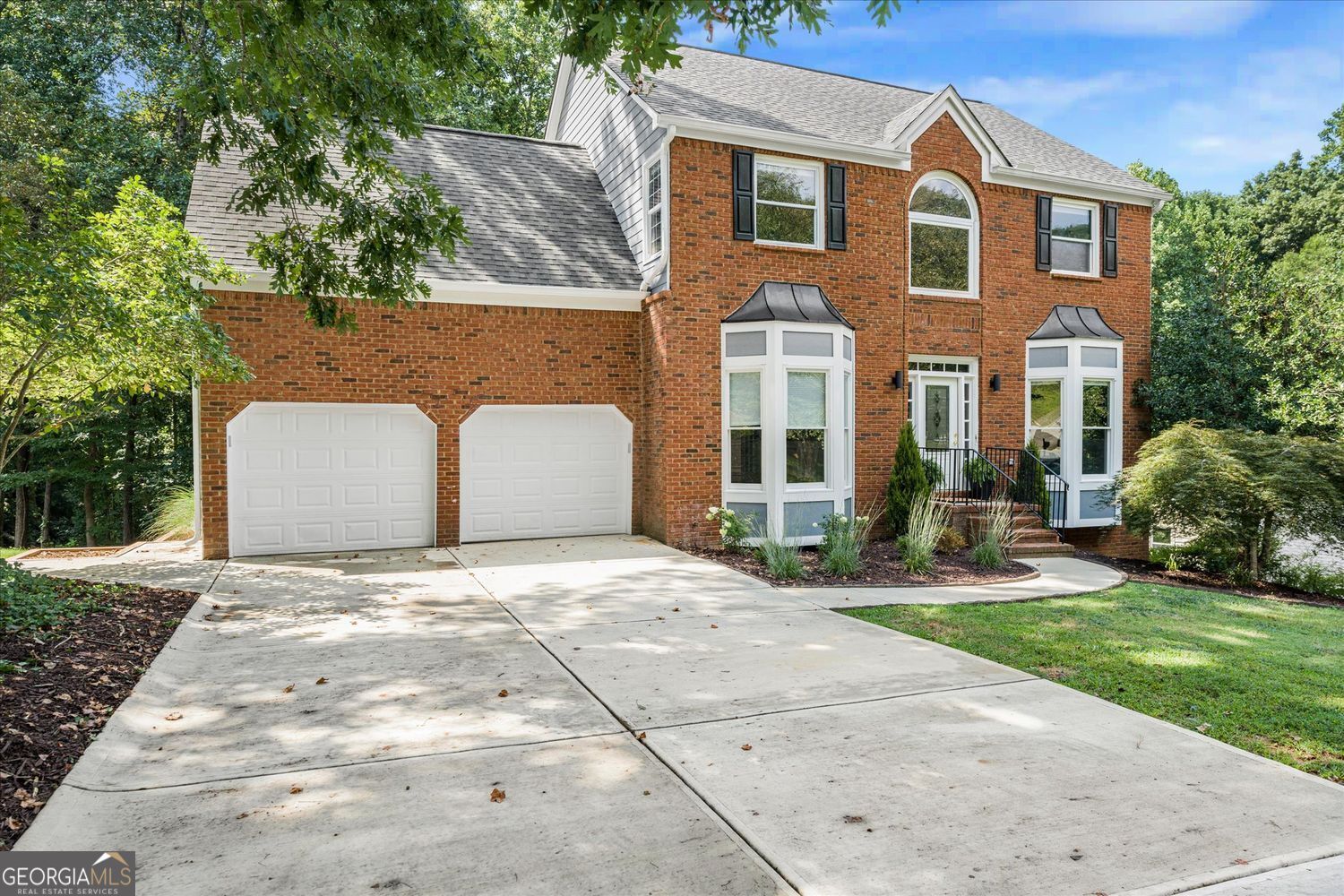 Two-story brick house with twin garage doors, bay windows, and a wide concrete driveway.