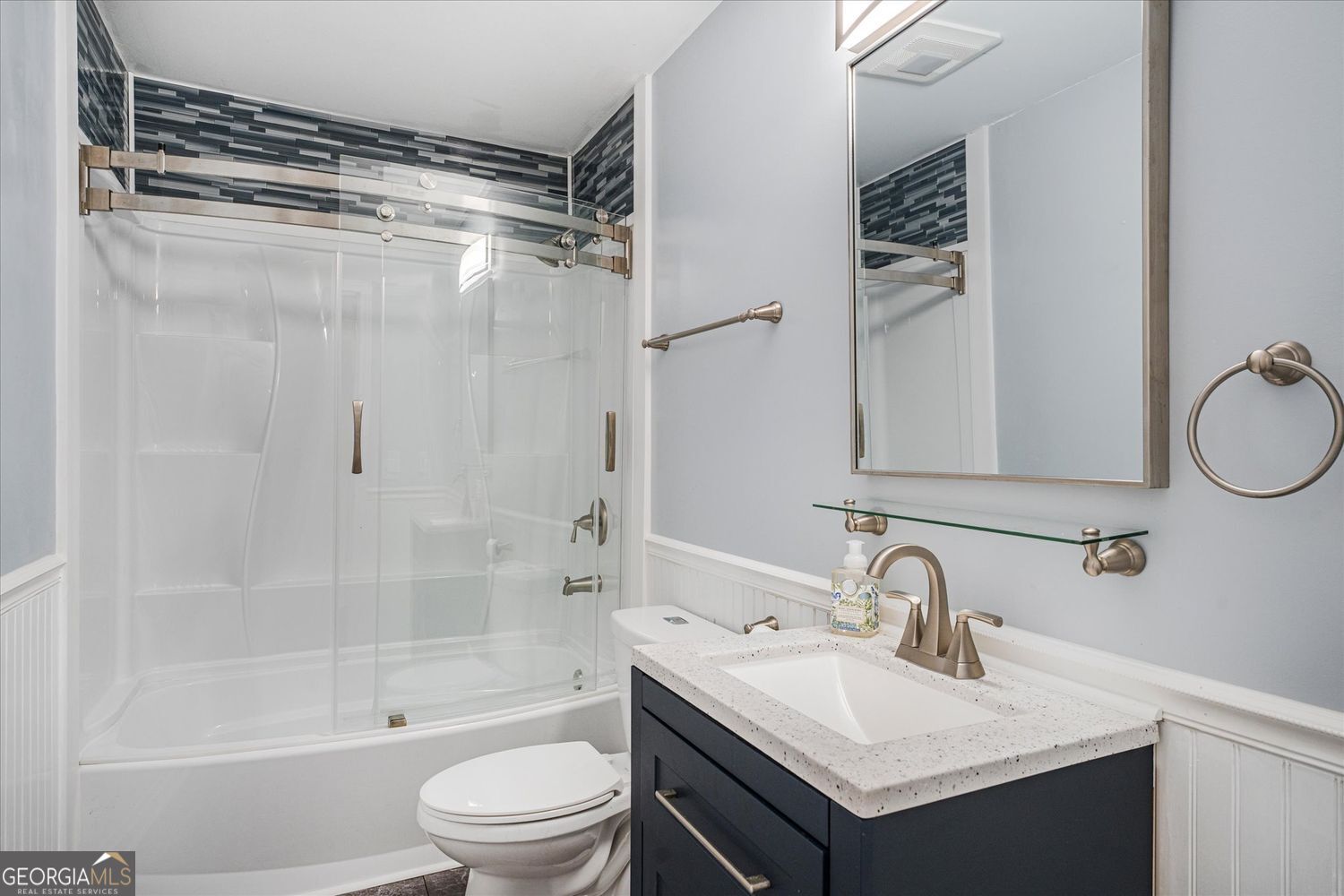 Bathroom with glass-enclosed tub and shower beside a dark vanity with a white countertop.