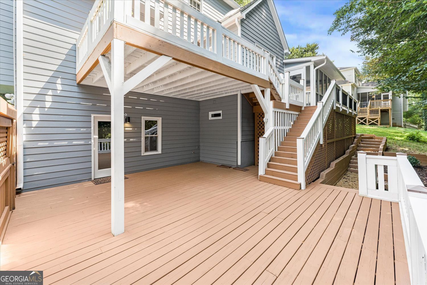 Spacious lower deck beneath a raised deck, with white-railed stairs beside gray siding.