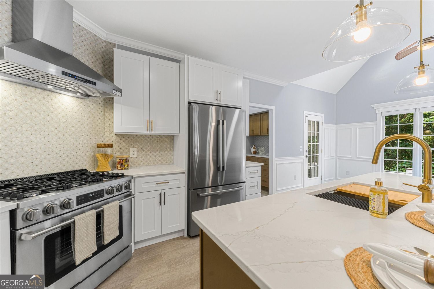 Kitchen with white cabinets, stainless steel appliances, patterned tile backsplash, and a large quartz island.