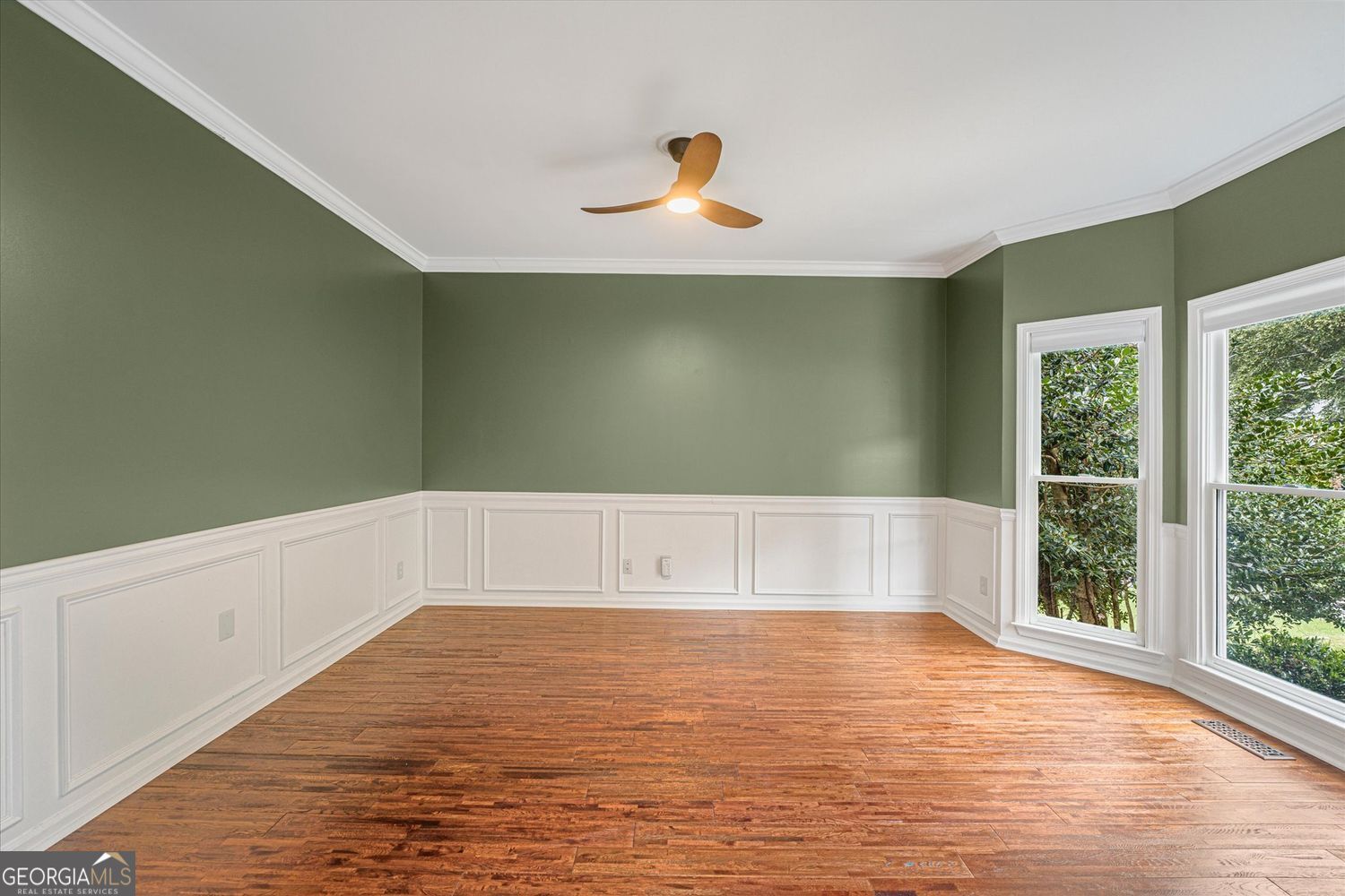 Empty room with green walls, white wainscoting, hardwood floors, and two tall windows.