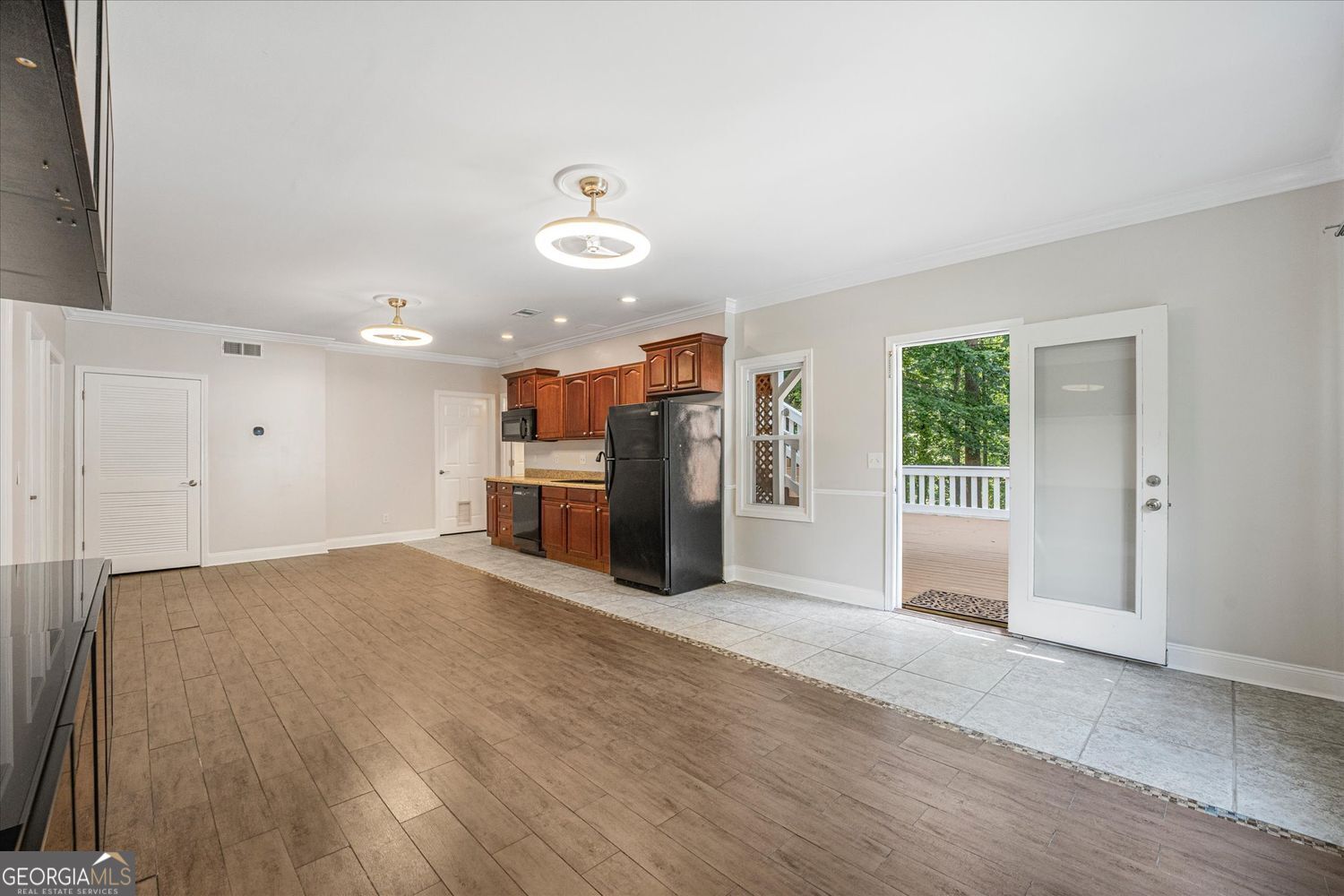 Kitchen with reddish-brown cabinets, wood-look flooring, and an open door to a tree-lined deck.