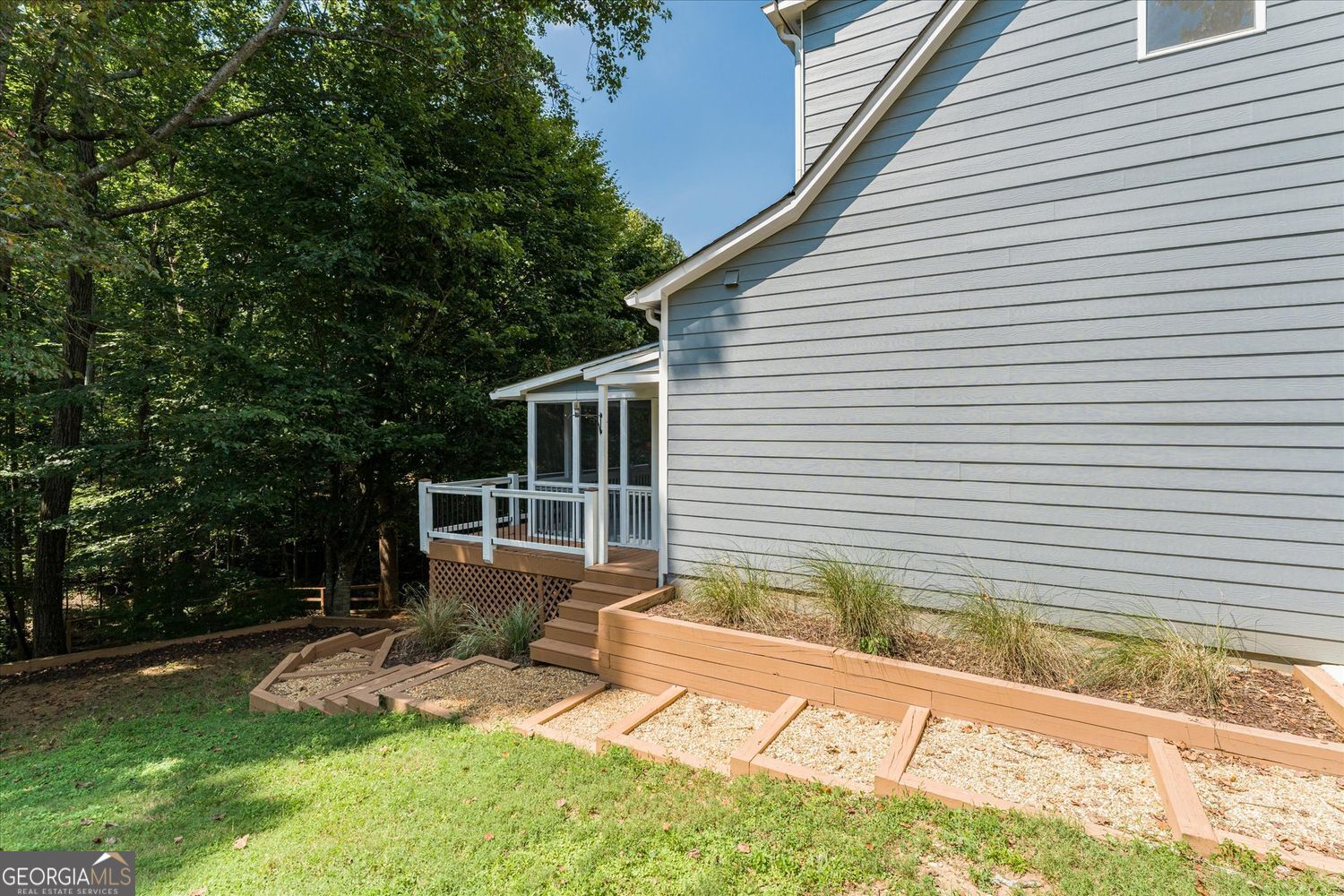 Rear exterior of a gray-sided home with a raised deck and wooded yard.