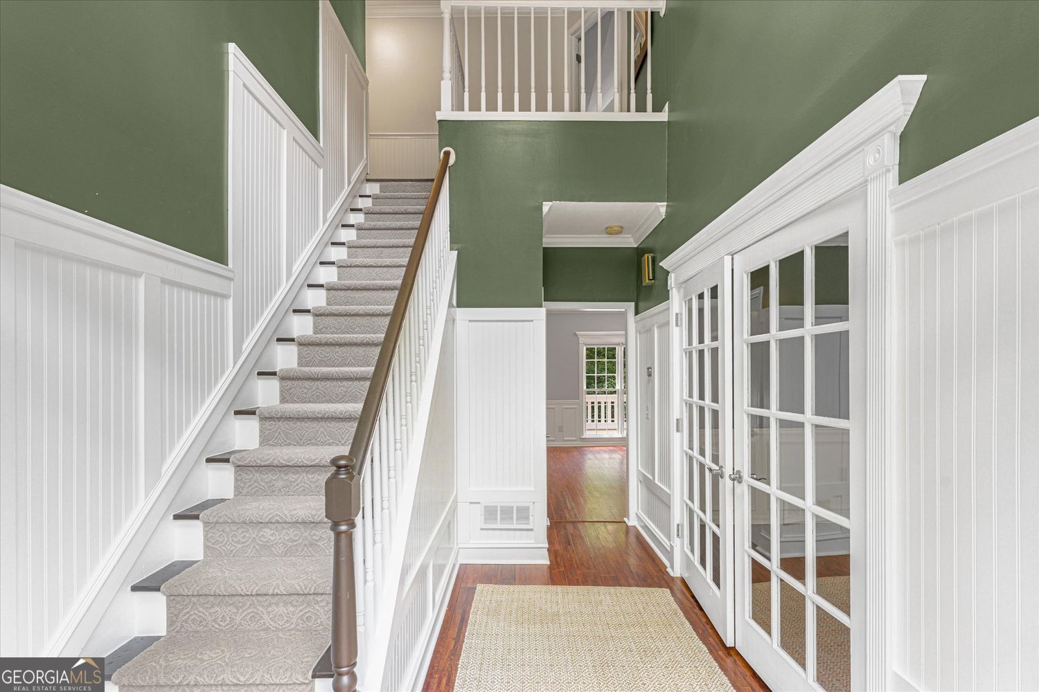 Foyer with a carpeted staircase, green walls, white wainscoting, and French doors.