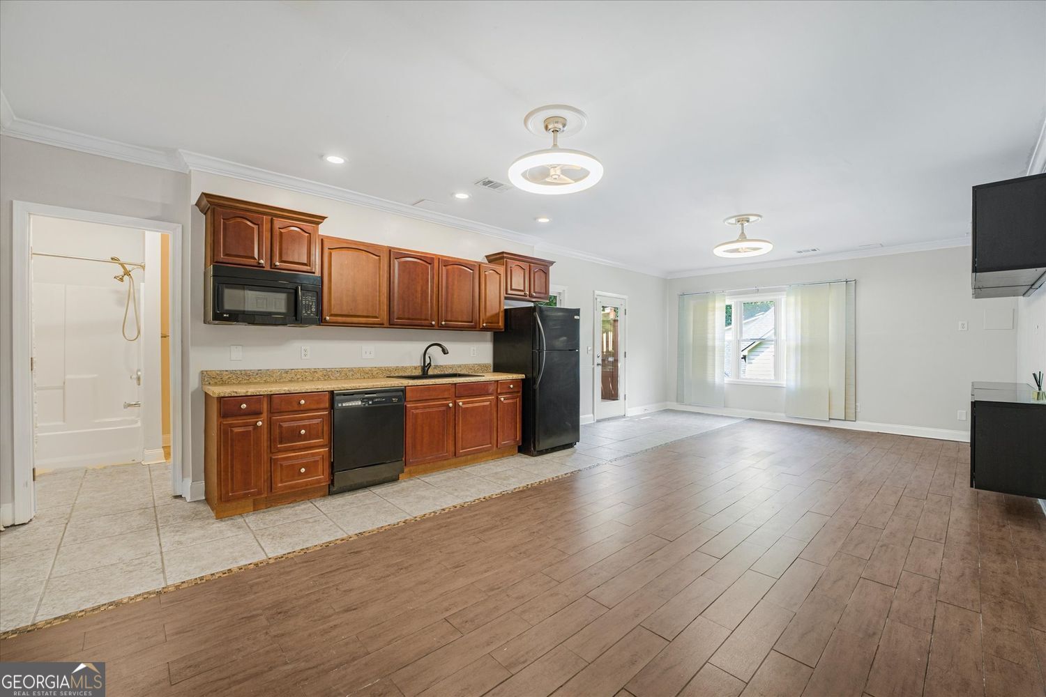 Kitchen with reddish-brown cabinets and granite counters opens to a spacious, mostly empty living area.