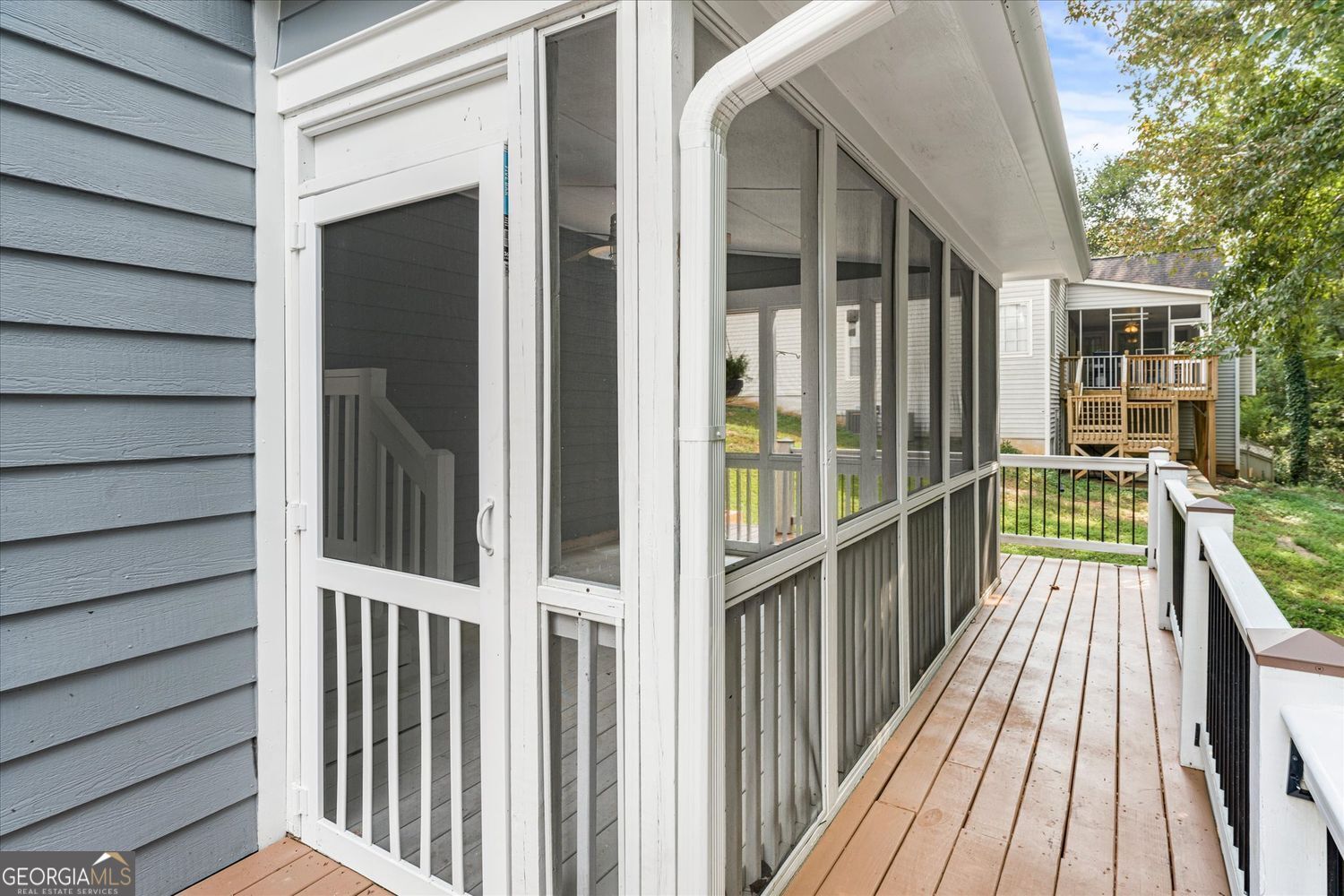 Wooden deck alongside a screened porch, with white railings and a grassy yard beyond.