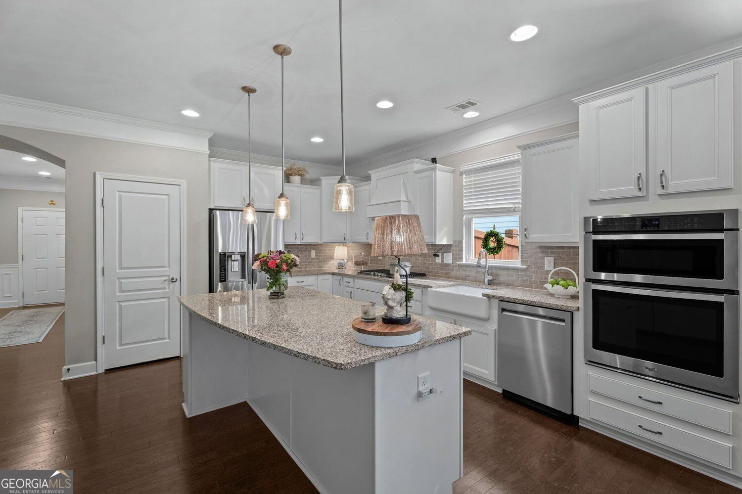 Kitchen with white cabinets, granite island, farmhouse sink, and stainless steel double ovens.