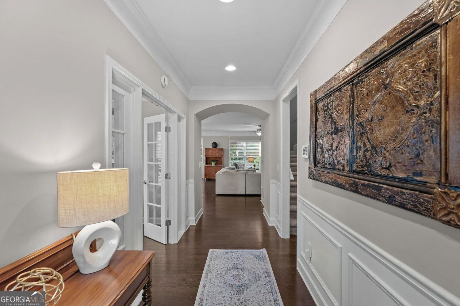 Furnished hallway with dark hardwood floors, a patterned runner, and an arched opening to the living room.