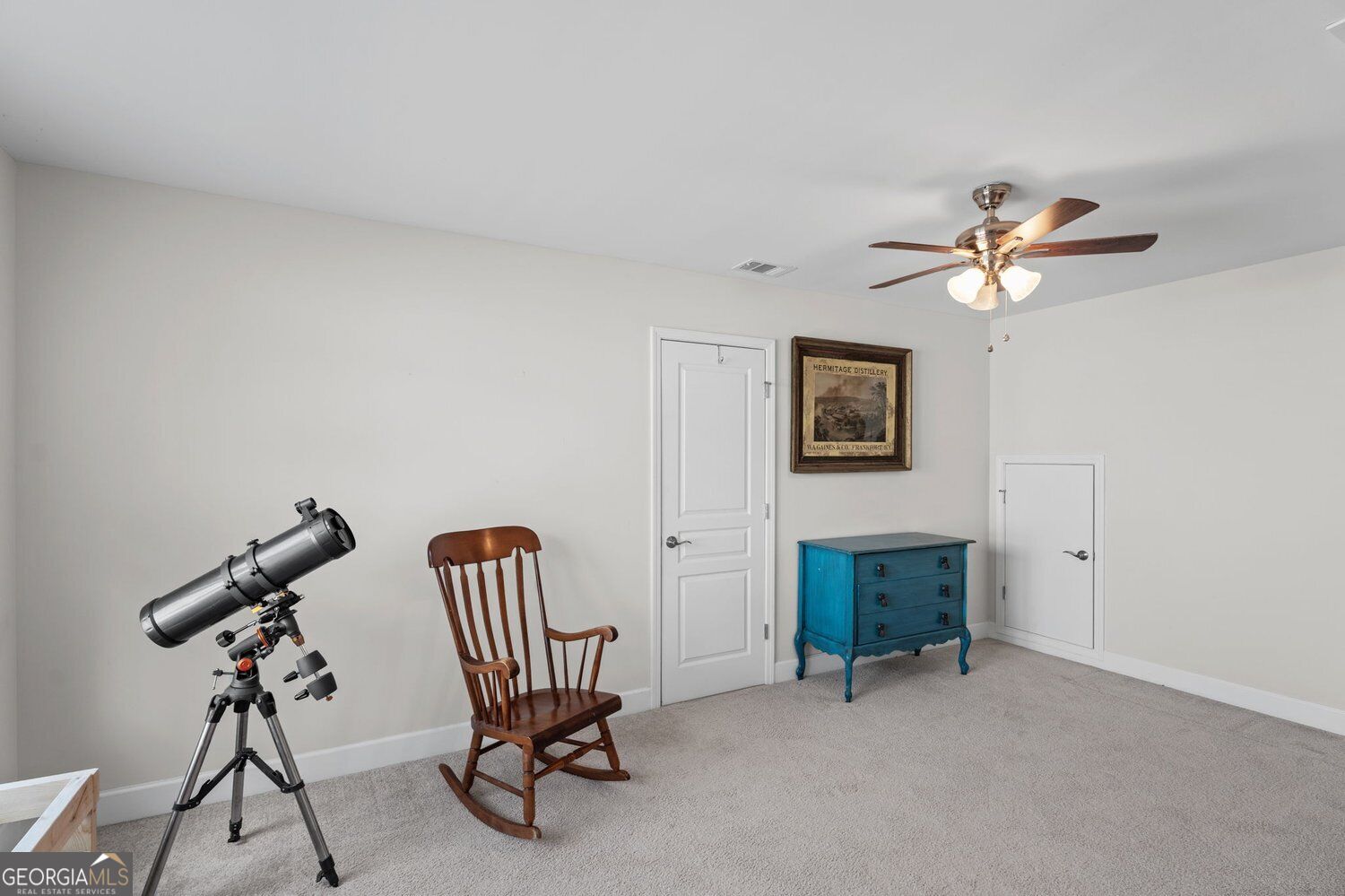 Carpeted room with a telescope, wooden rocking chair, and blue chest of drawers.