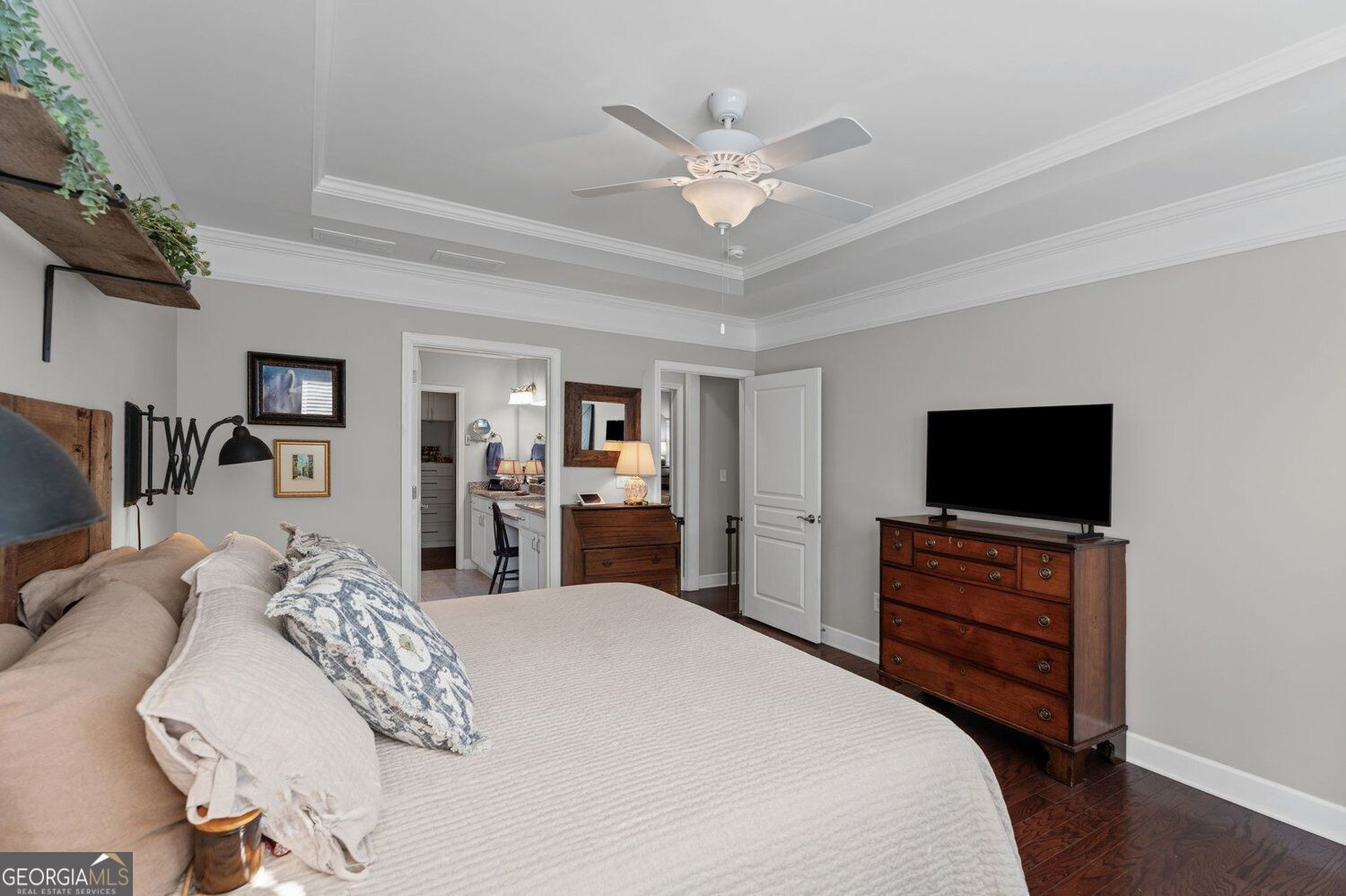 Bedroom with a tray ceiling, ceiling fan, hardwood floors, and a wooden dresser with a television.