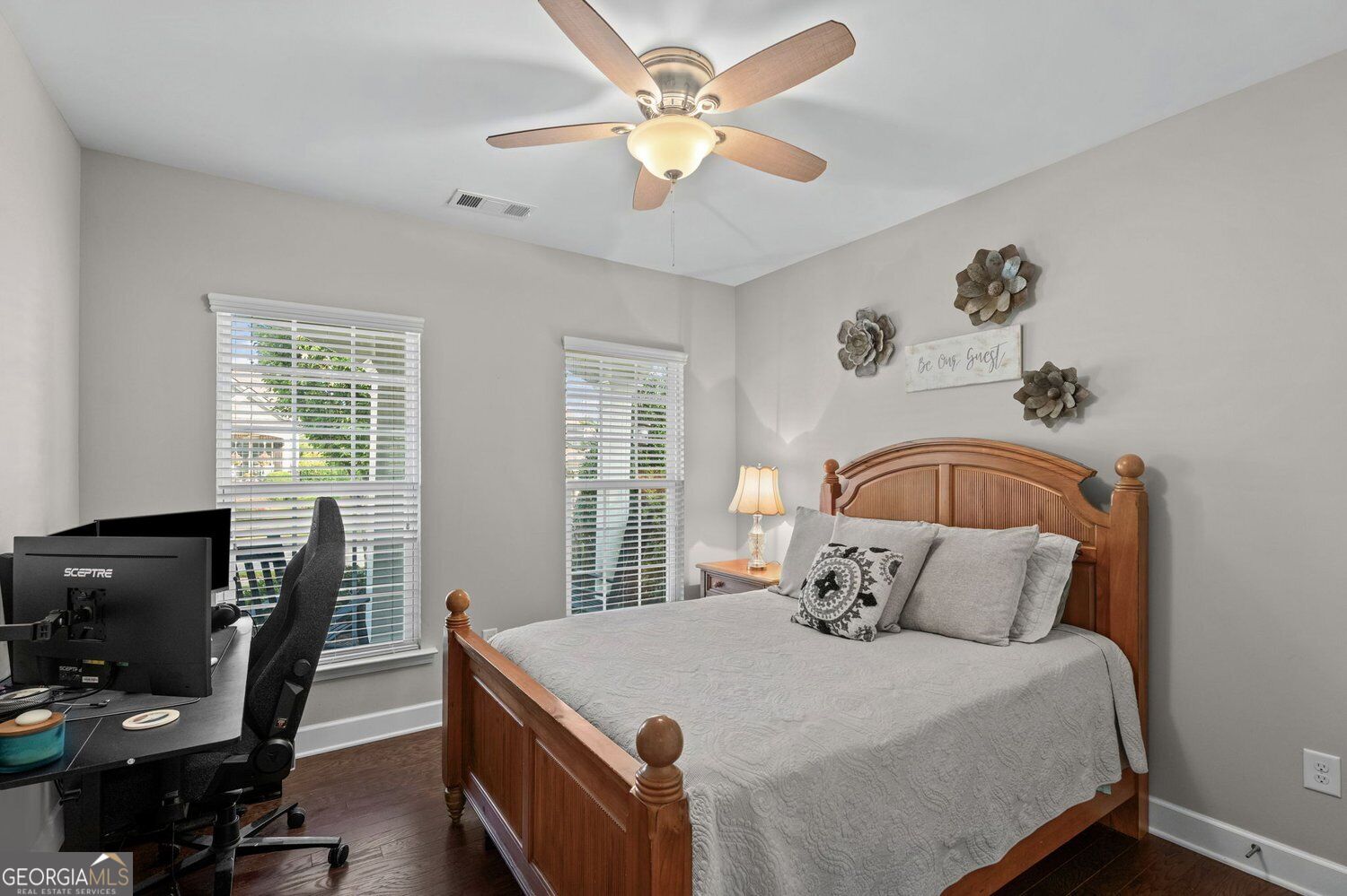 Bedroom with a wooden bed, gray bedding, and a desk beside two windows.