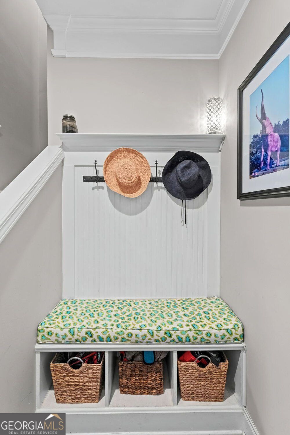Mudroom bench with a patterned cushion, woven baskets, and hats on wall hooks.