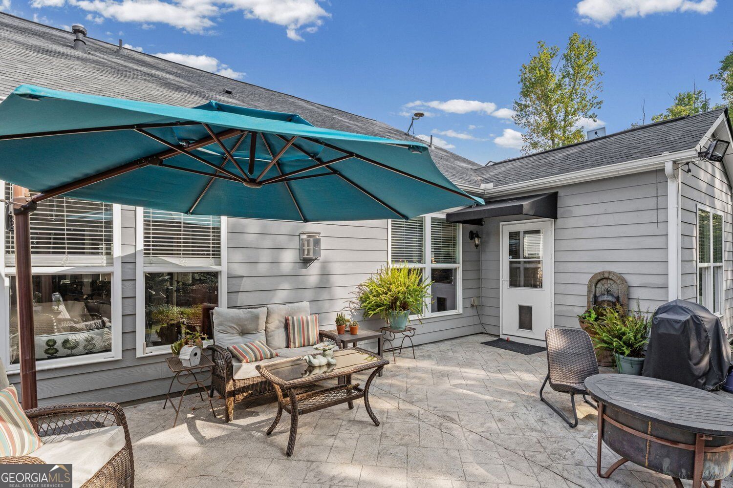 Furnished stone-paver patio with wicker seating beneath a large teal umbrella.
