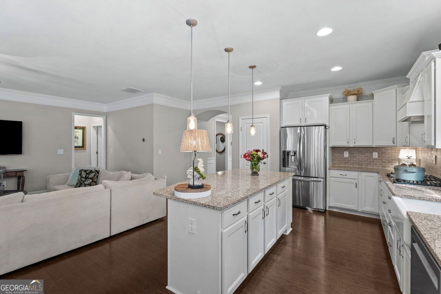 Open kitchen with a granite island and white cabinetry adjoining a living area with a light sectional sofa.