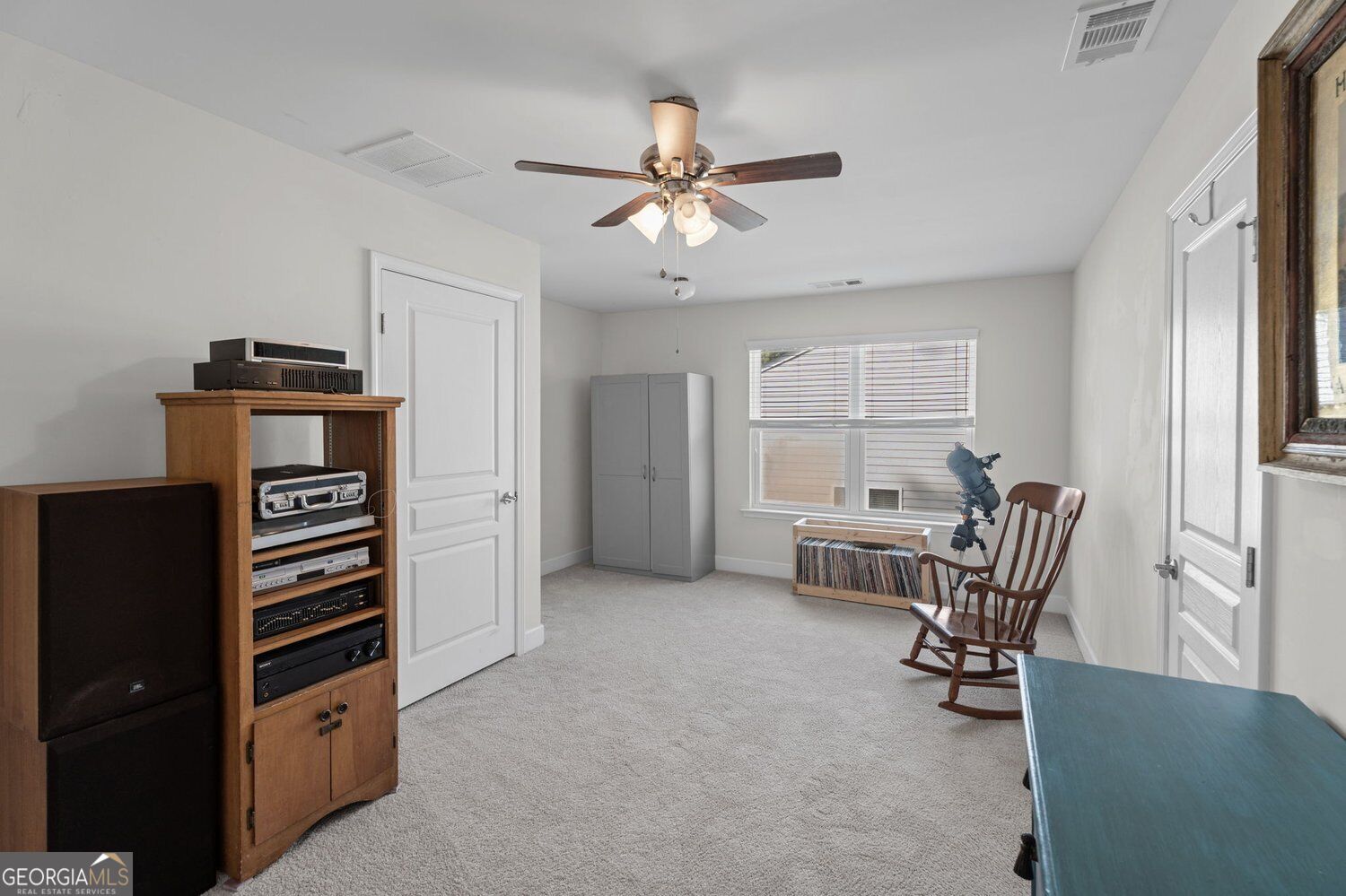 Carpeted bonus room with a telescope beside a wooden rocking chair and media cabinet.