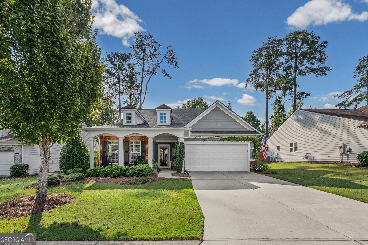 Gray home with brick porch columns, two dormers, and an attached two-car garage.