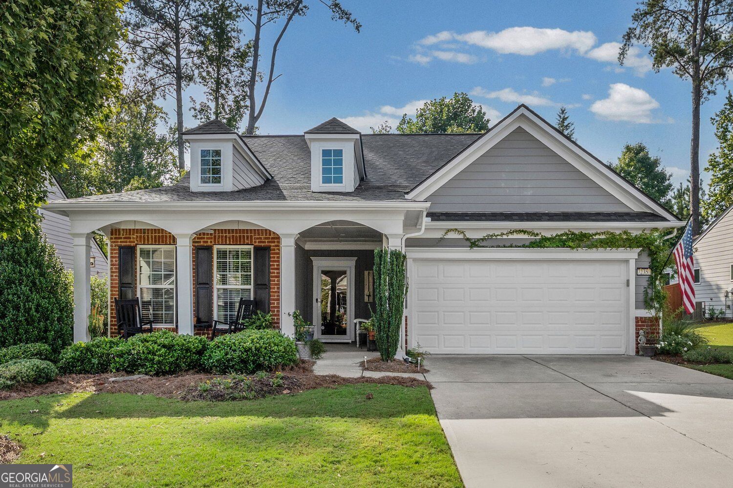 Gray and brick home with a covered porch, dormer windows, and a two-car garage.