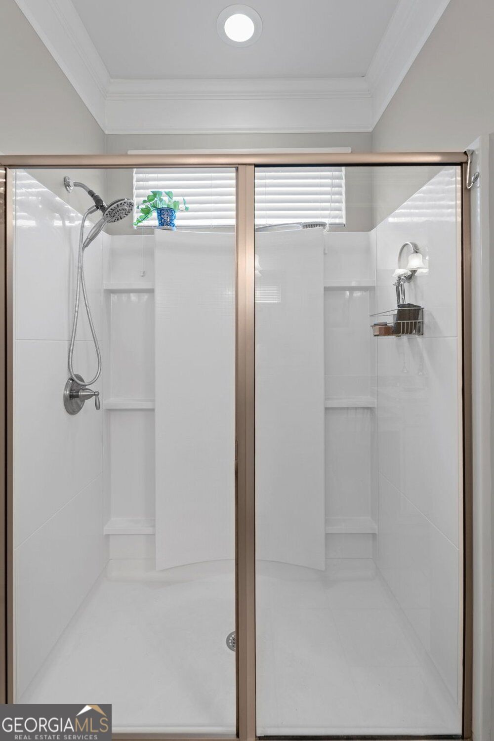 Walk-in shower with sliding glass doors, two showerheads, built-in shelves, and a high window.